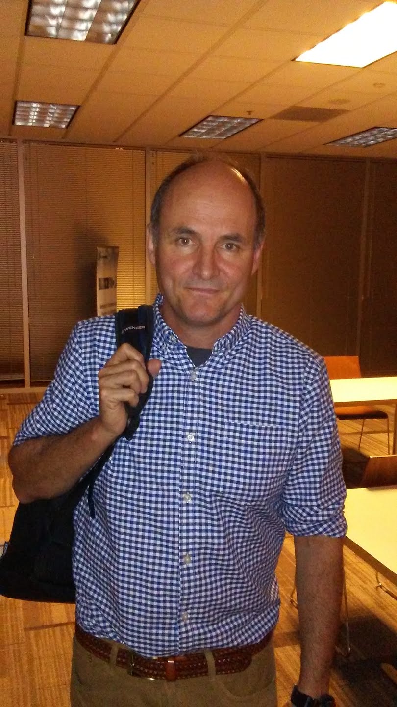 Michael Kerrisk standing in a meeting room, wearing a checkered shirt and carrying a shoulder bag.