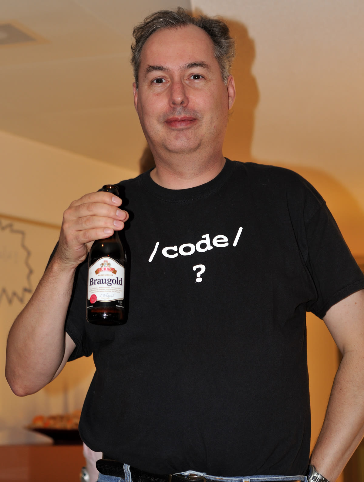 Vim 创始人 Bram Moolenaar 于 2007 年身穿印有代码的黑色 T 恤，手里拿着一个瓶子。