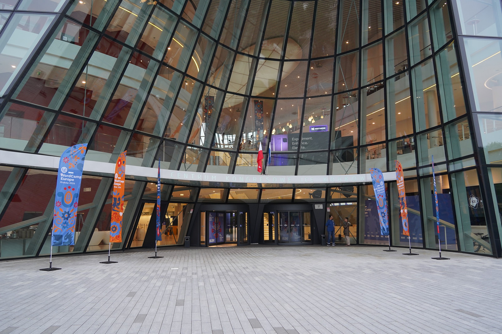 克拉科夫 WordCamp Europe 2026 会场入口，玻璃幕墙前立着 WordCamp 旗帜。