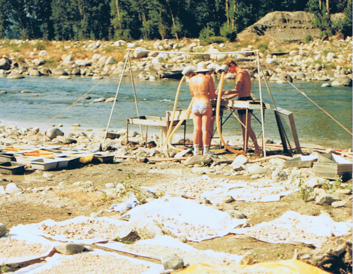 Two paleontologists operate a water-powered wash-sieving table during fieldwork in Spain, with sediment samples drying in the foreground.