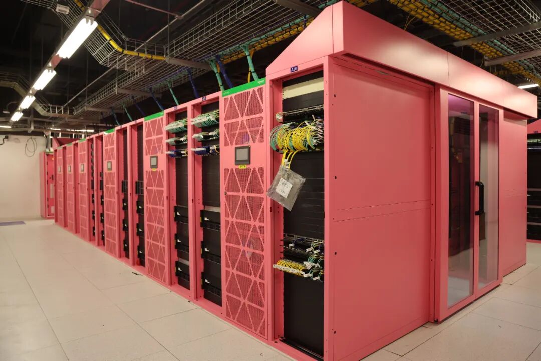 A row of vivid pink computing cabinets with exposed network cables inside the Baicheng Advanced Intelligent Computing Center in Jilin, China.
