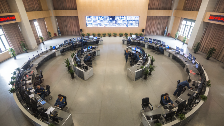 Baosteel blast-furnace operators seated at concentric control desks beneath a wall of live production screens.