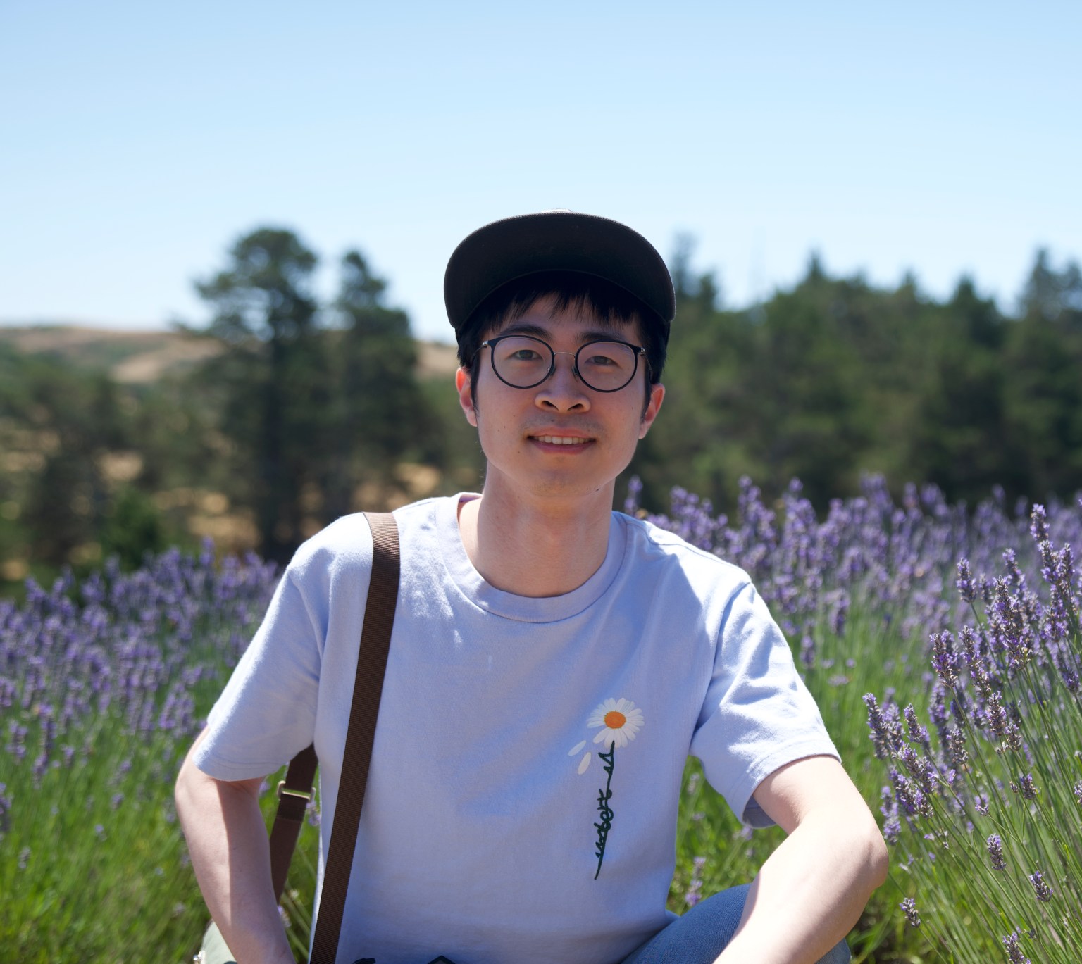 Portrait of ByteDance researcher Haibin Lin wearing glasses and a cap in a field of purple flowers.
