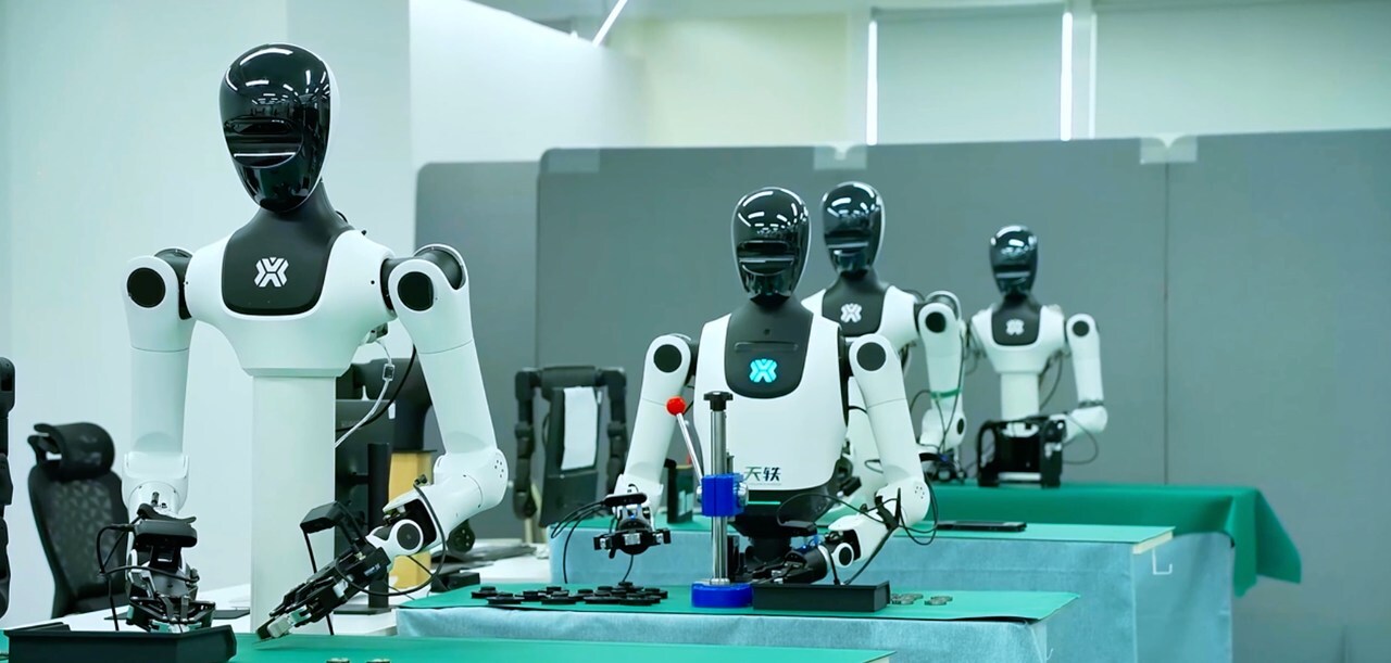 四台黑白配色的天工人形机器人在实验室铺有绿色台垫的精密操作工作台前作业。