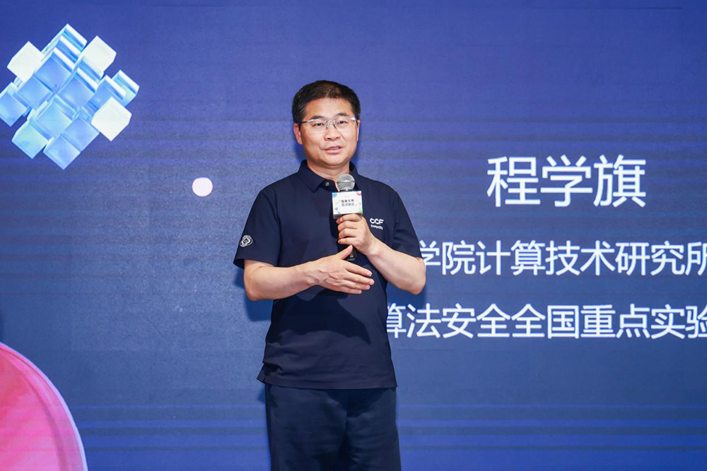 Cheng Xueqi speaking into a handheld microphone on a blue conference stage.