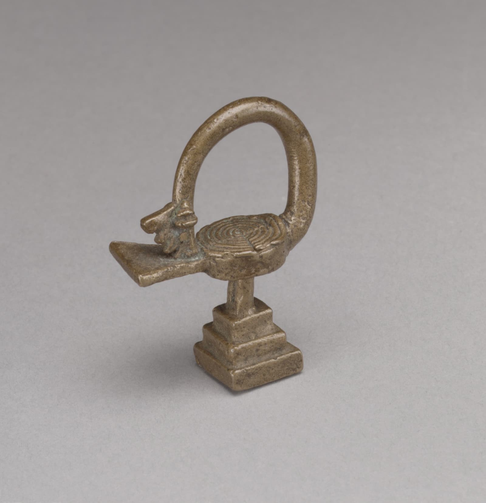 Small brass bird sculpture on a stepped base, its long looped neck turning its beaked head back toward its tail.