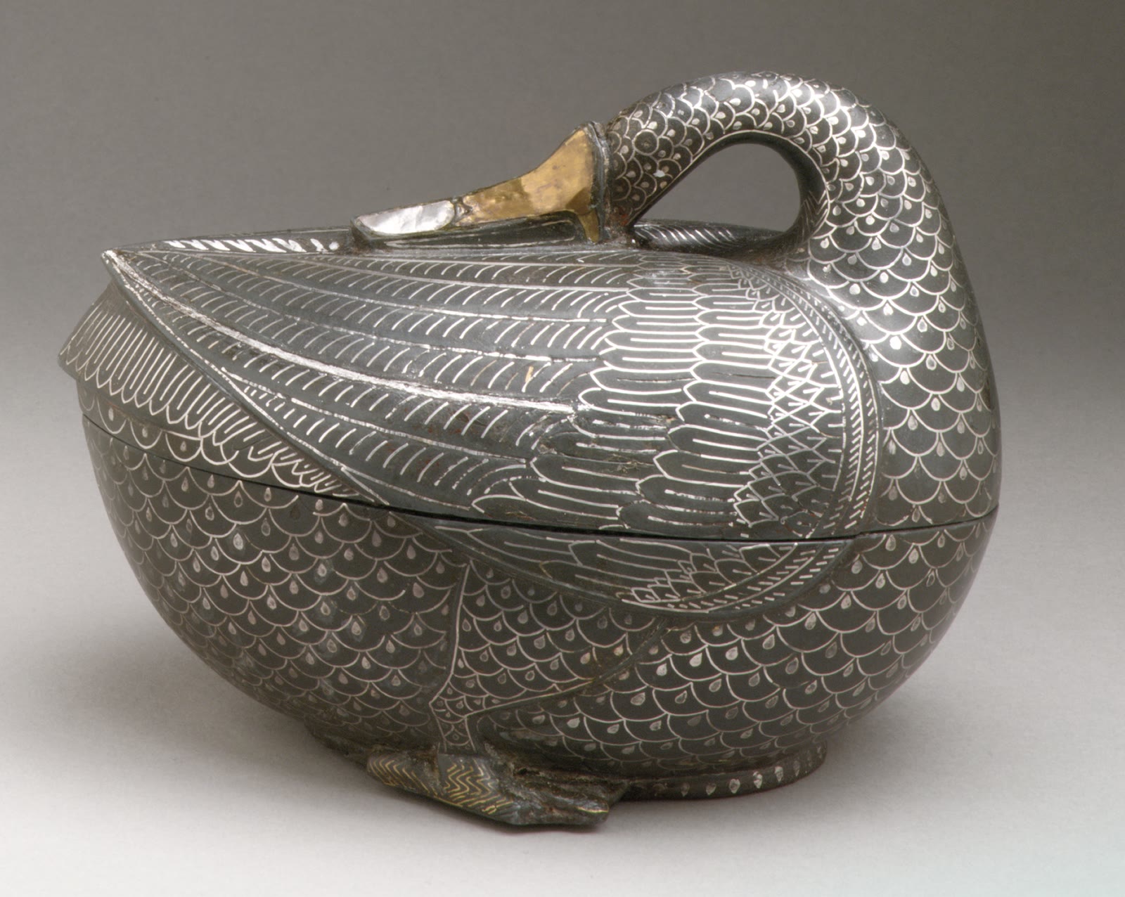 A small black metal box shaped like a resting duck, with bright silver and brass inlay articulating its layered feathers, folded wings, curved neck, and beak.