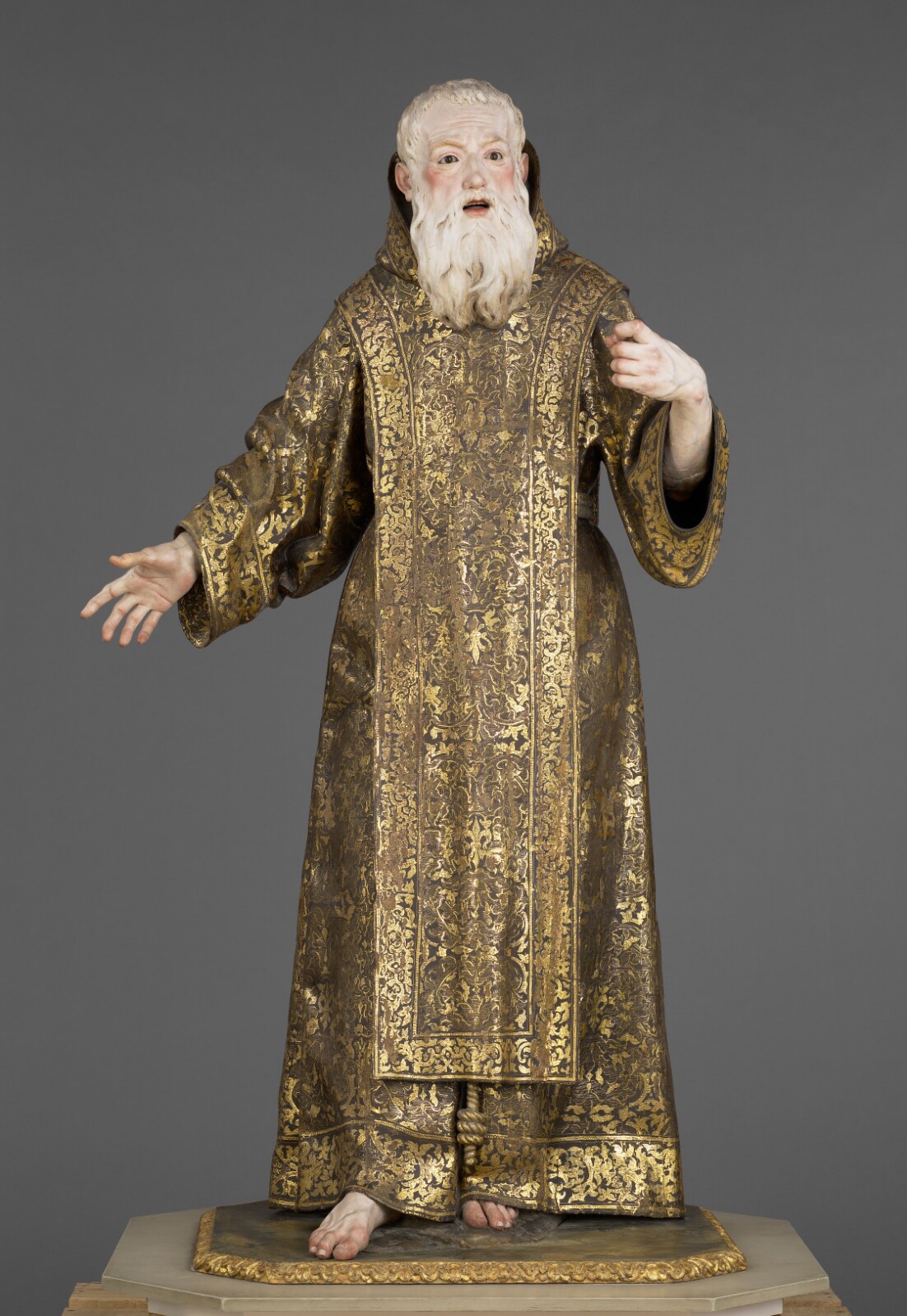 Luisa Roldán's life-size polychrome wooden Saint Ginés, an elderly bearded figure in a black-and-gold brocaded robe, stands with mouth open and arms outstretched.