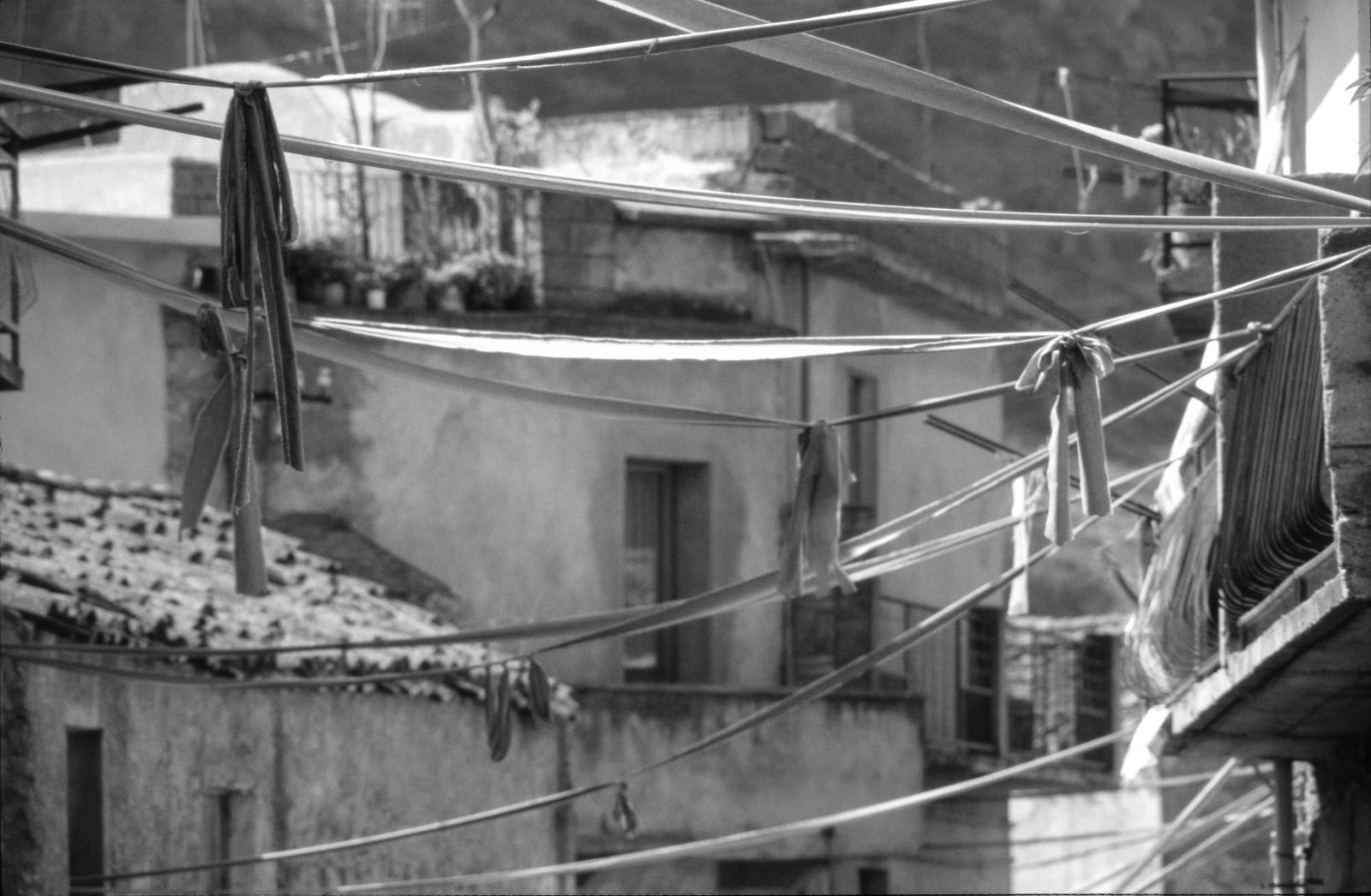 Black-and-white archival photograph of long ribbons hanging between stone buildings in Ulassai during Maria Lai's 1981 collective artwork Legarsi alla montagna.