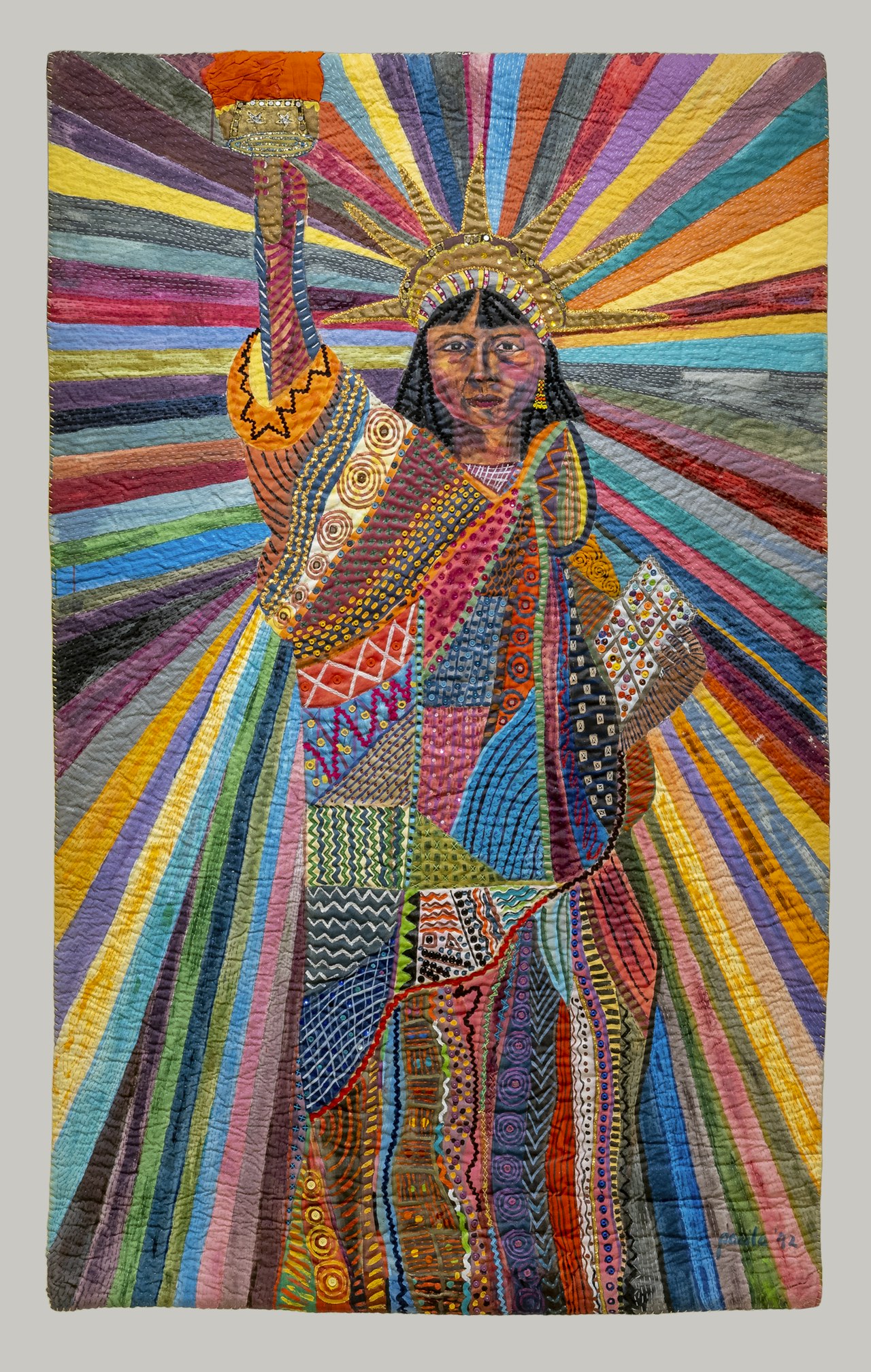 Pacita Abad's L.A. Liberty, a tall stitched textile painting of a front-facing brown-skinned Liberty raising a flame amid radiant bands of saturated color.