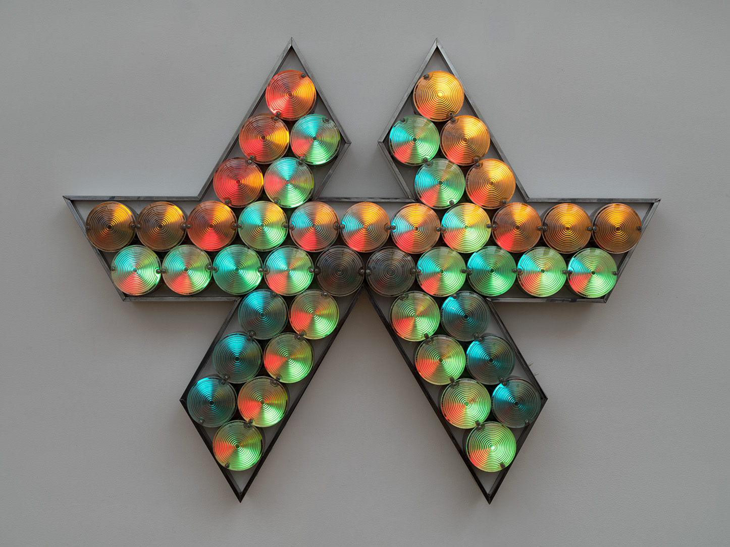 Tom Lloyd's Clavero, an angular aluminum light sculpture whose circular lenses glow in red, green, blue, amber, and white against a pale wall.