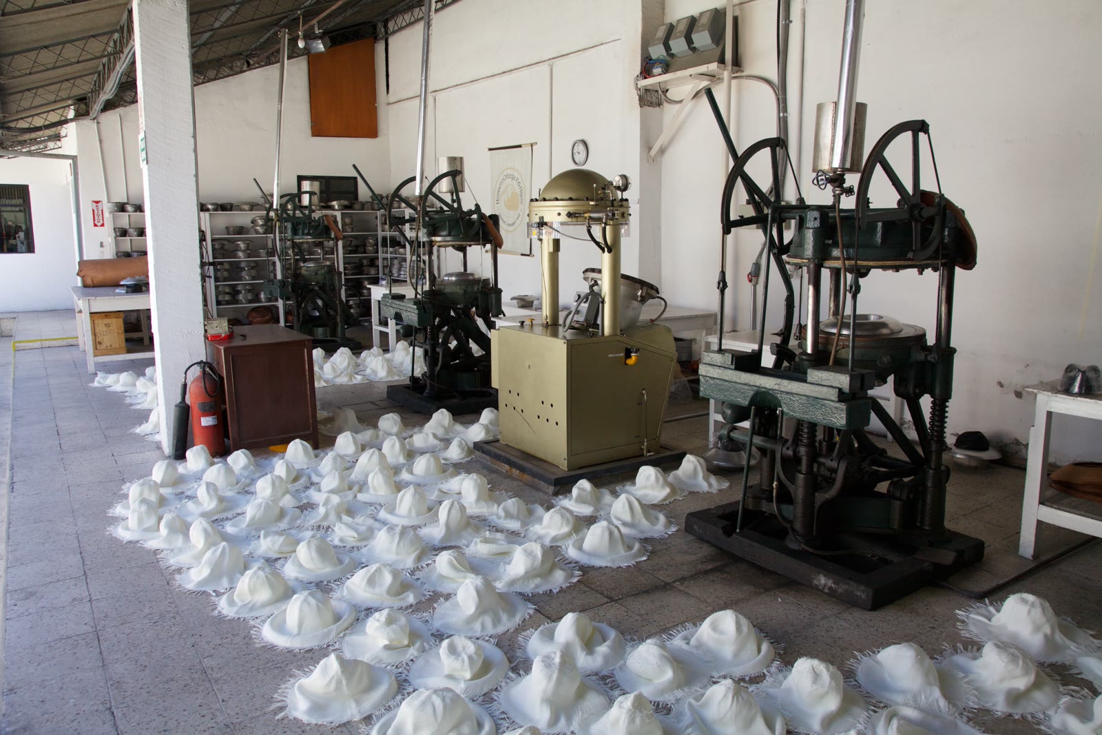 Unfinished white toquilla-straw hats lie beside green blocking presses on the floor of the Homero Ortega hat factory in Cuenca.