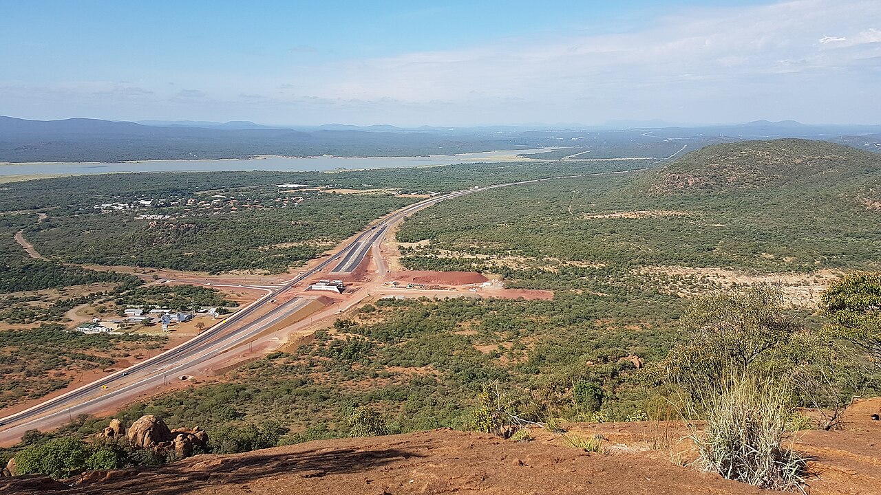 从 Kgale Hill 的岩石坡面越过 A1 公路，远望哈博罗内水库与低矮青山。