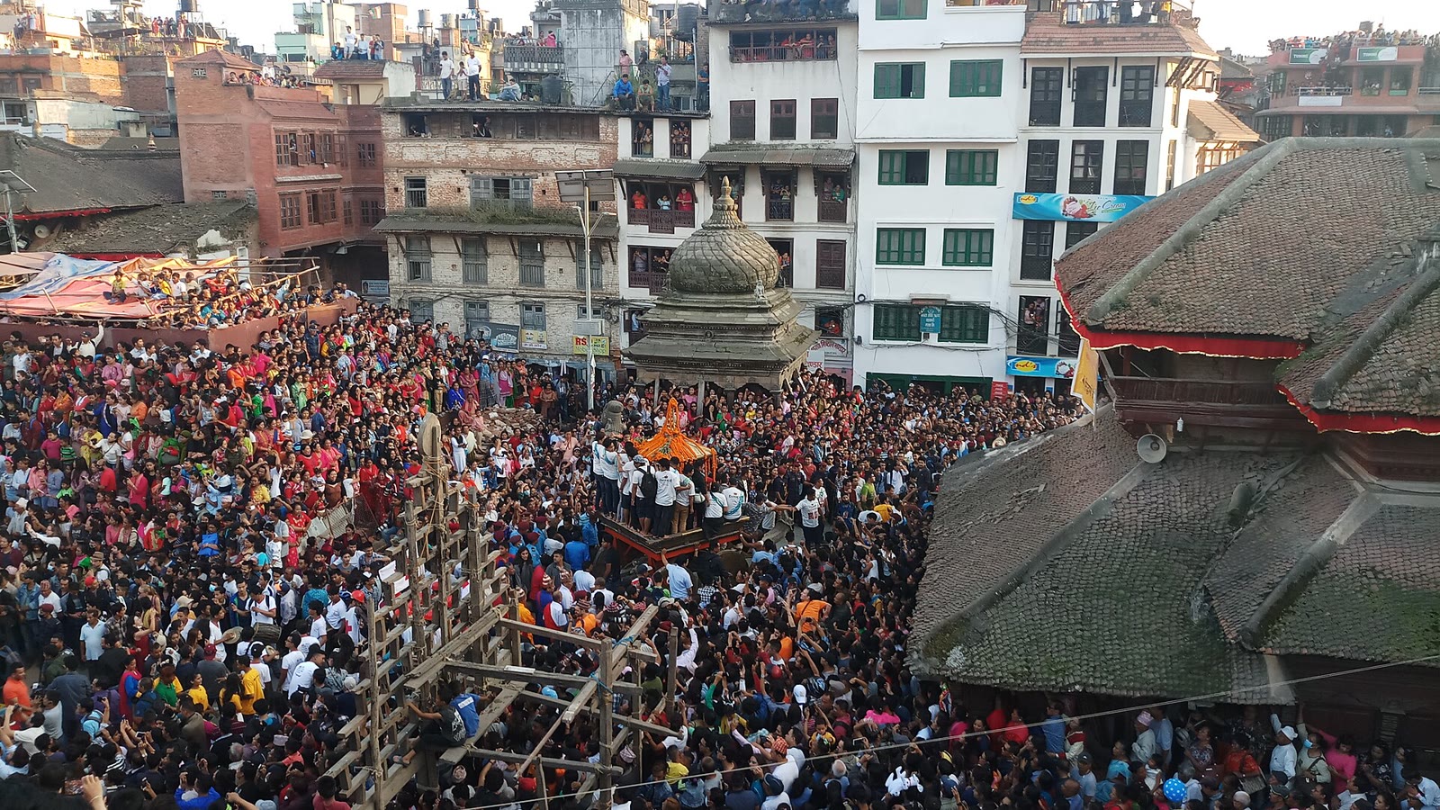An Indra Jatra chariot surrounded by devotees in Kathmandu Durbar Square, with the square's brick and timber buildings behind it