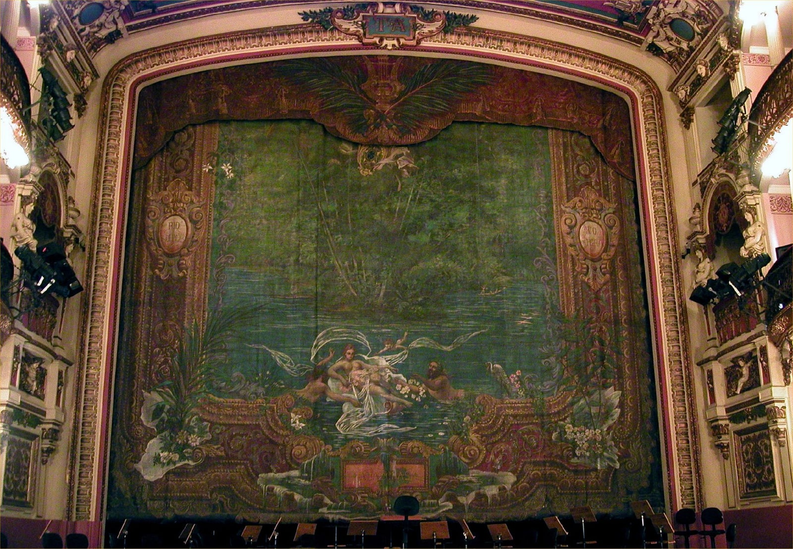The stage of Teatro Amazonas in Manaus, framed by gilded side balconies and Crispim do Amaral's painted Meeting of the Waters curtain.