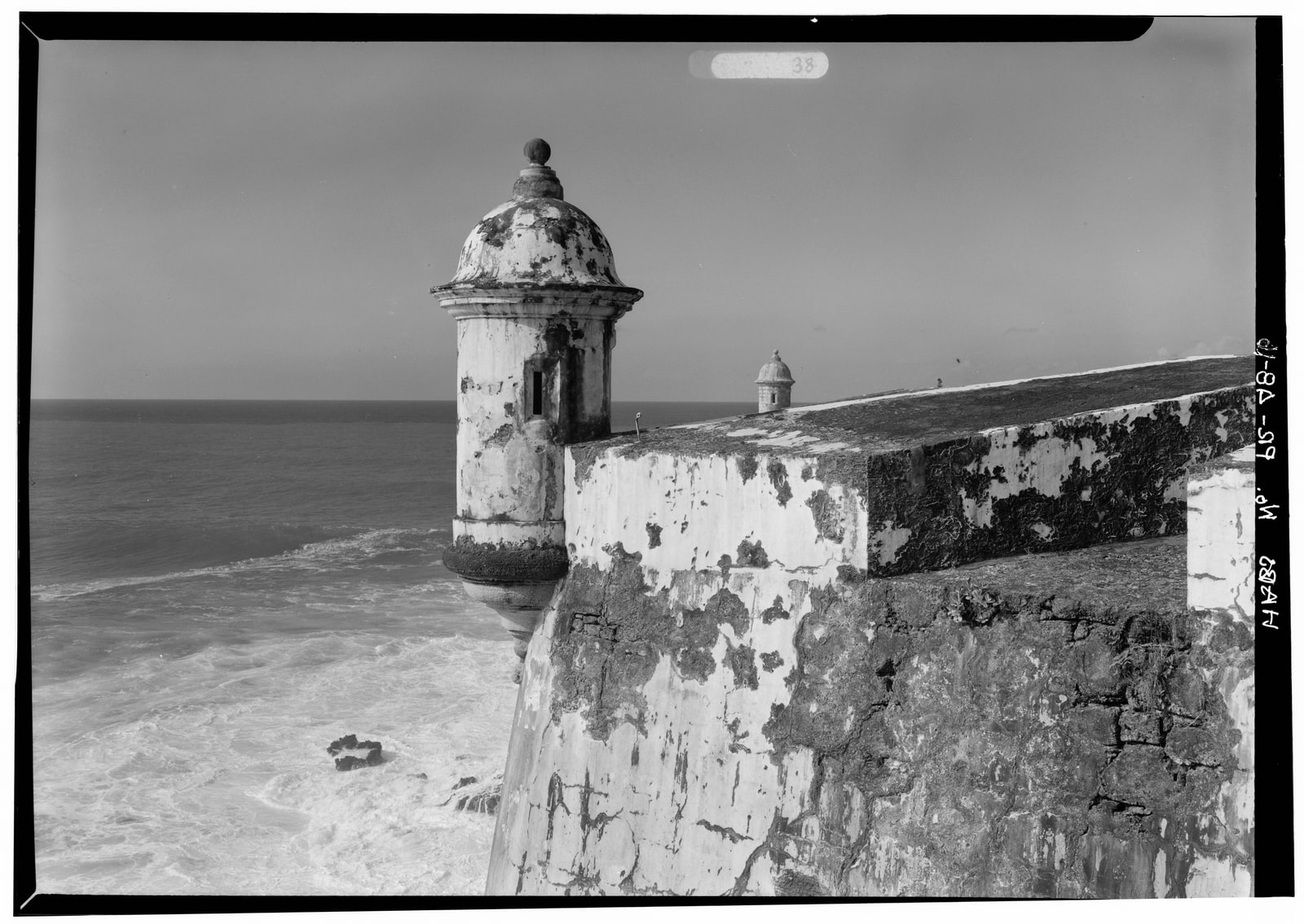 Black-and-white archival photograph of a domed garita projecting from El Morro's weathered walls above Atlantic surf, with a second sentry box in the distance.