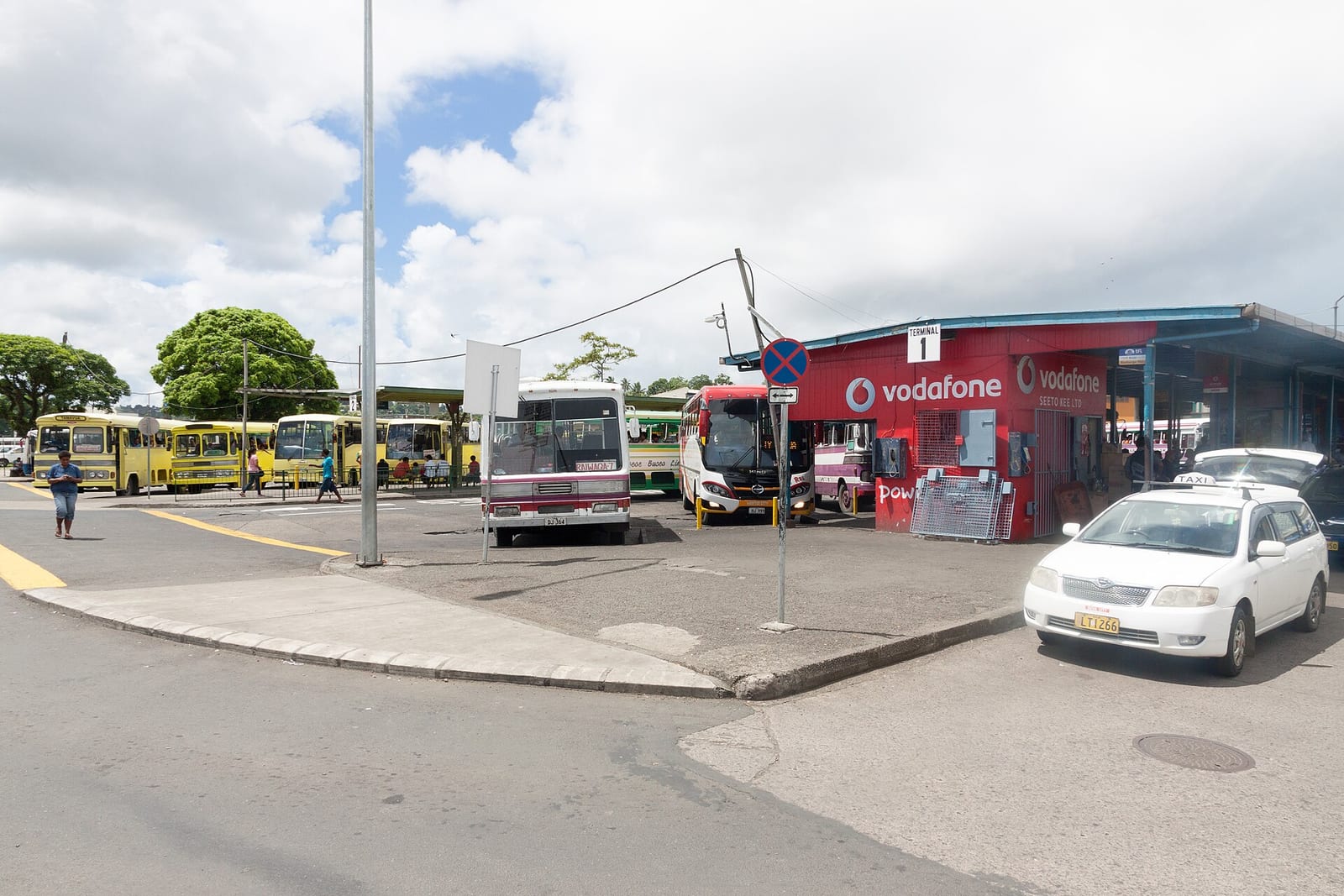 Buses line several bays at Suva's central bus station beside a terminal building and taxi rank.