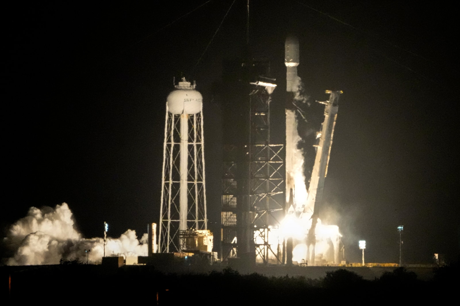 A Falcon 9 rocket lifts off at night from Kennedy Space Center amid bright exhaust and smoke.