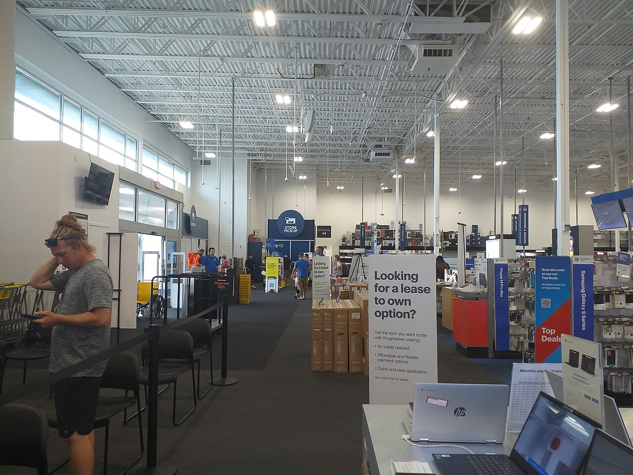 佛罗里达州巴拿马城一间 Best Buy 门店内部，顾客、员工、商品陈列、收银台与到店取货标识均在画面中。