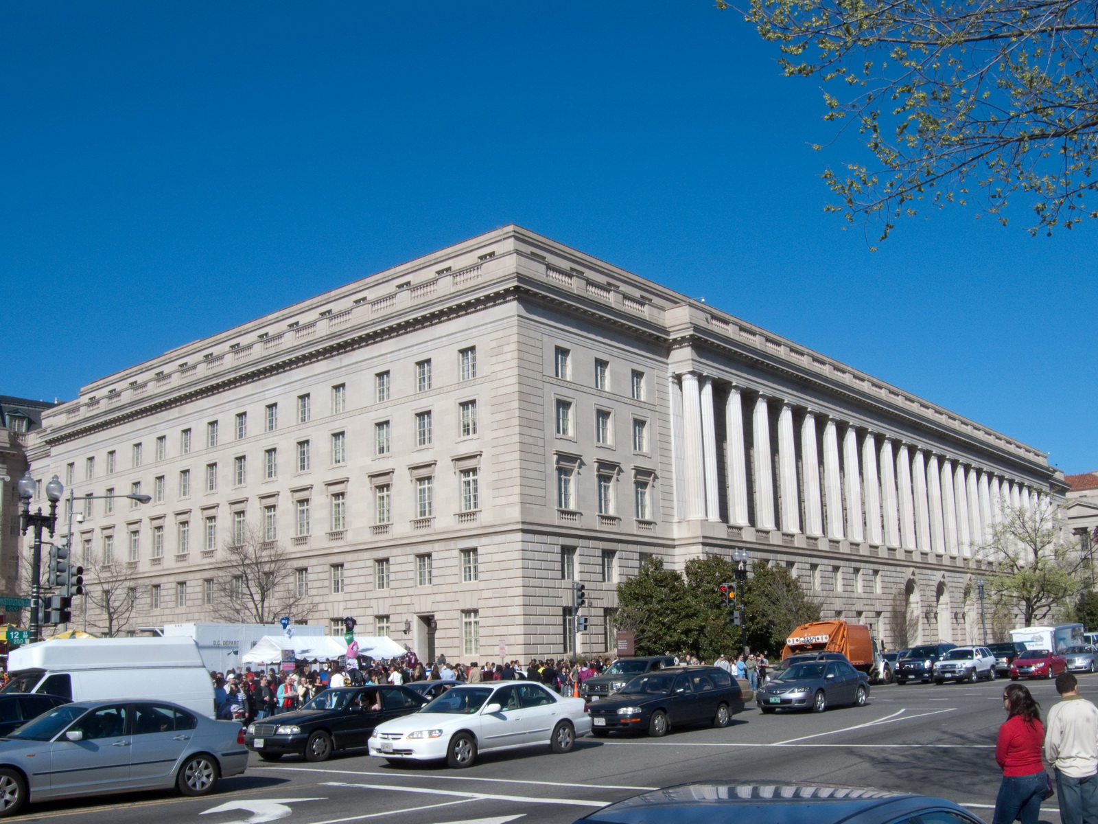 The stone facade and columns of the Internal Revenue Service headquarters on Constitution Avenue in Washington, D.C., with traffic and pedestrians in front.