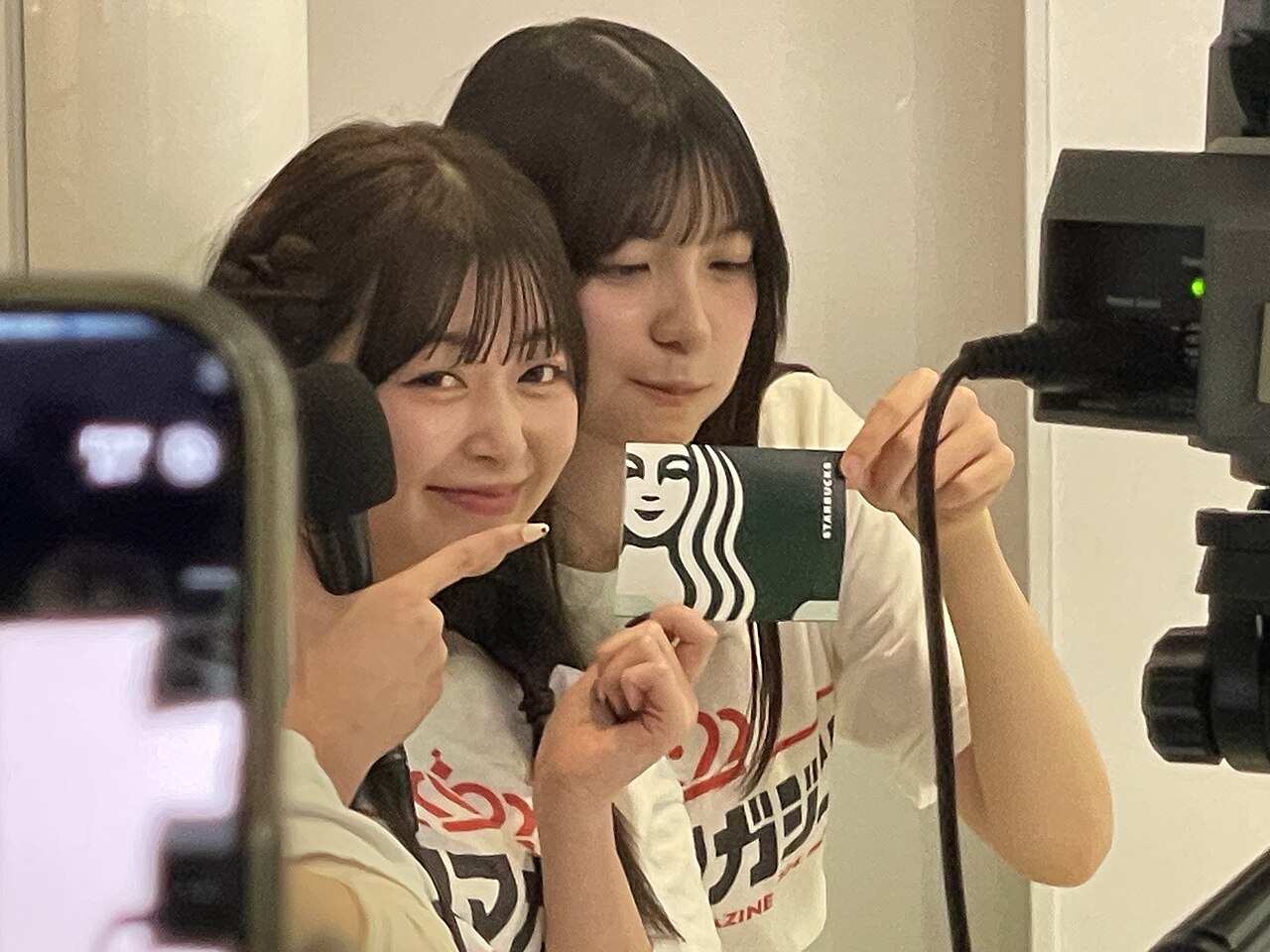 东京涩谷一间录音室里的两位电台主持人朝镜头展示一张绿色星巴克礼品卡。