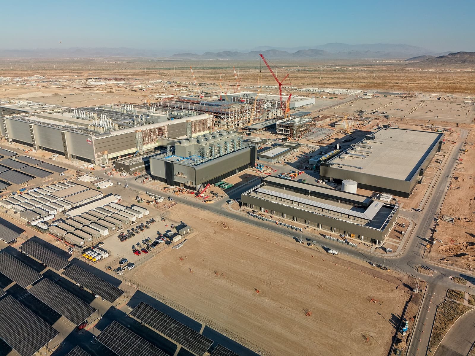 Aerial view of the sprawling TSMC Fab 21 semiconductor construction site in Phoenix, with cranes, unfinished buildings, and desert roads.