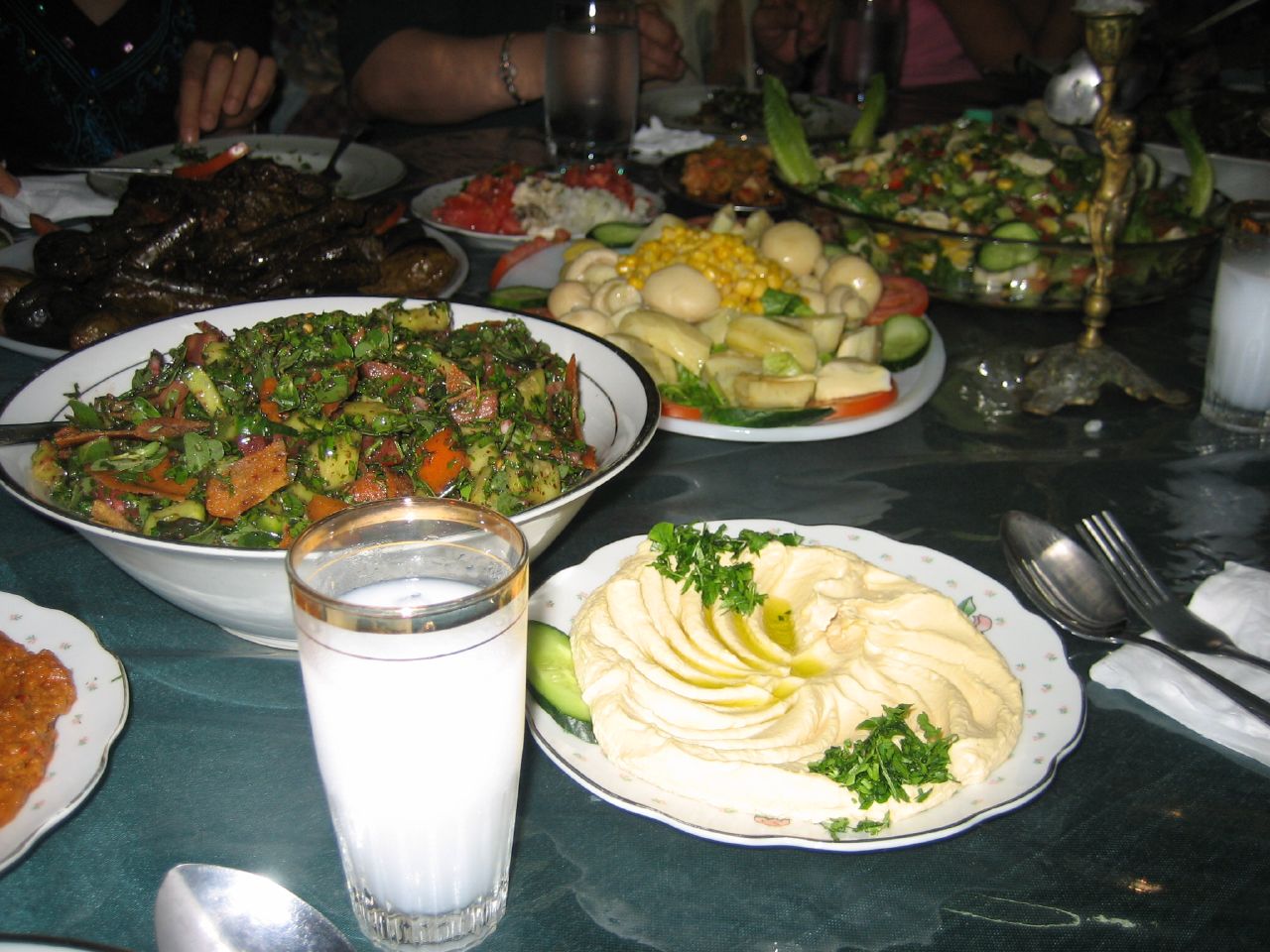 拥挤的 mezze 餐桌上，一只盛着浑白亚力酒的高杯立在鹰嘴豆泥、切碎沙拉、腌渍蔬菜与酿葡萄叶旁。