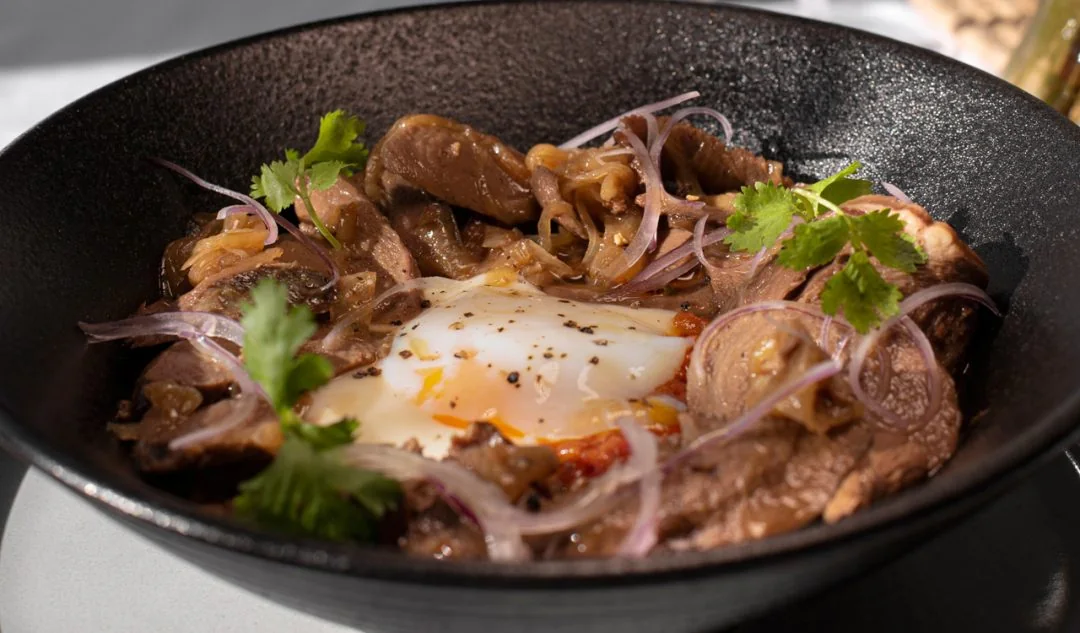 Beef, onions, herbs, and a soft-cooked egg served in a shallow black bowl at Táva Comedor in Asunción.