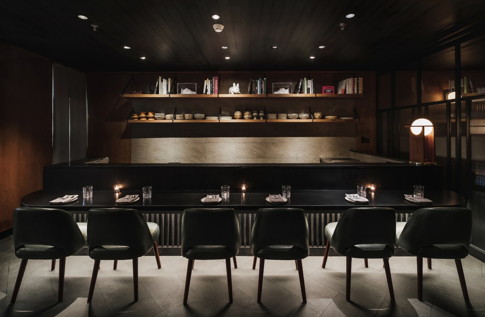 August Jakarta's dark chef's counter set with six place settings in front of the open pastry kitchen.