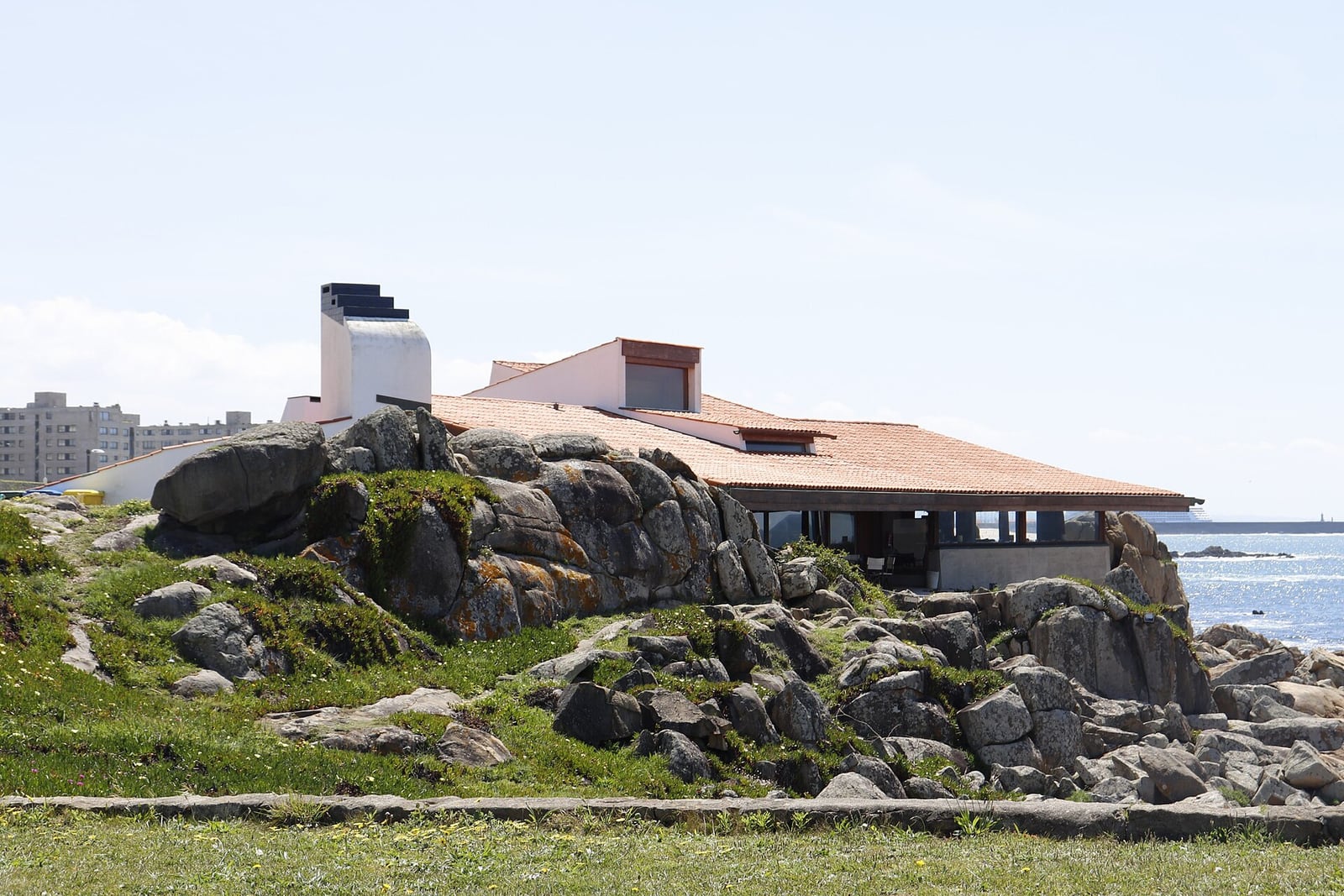 Casa de Chá da Boa Nova's low red-tiled roof and white chimney nested among granite rocks beside the Atlantic at Leça da Palmeira.