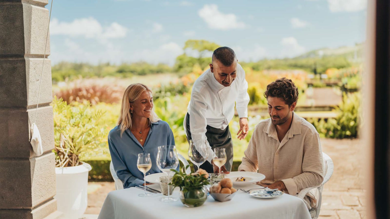 A server presents a plated lunch course to two guests seated at Le Château de Bel Ombre.