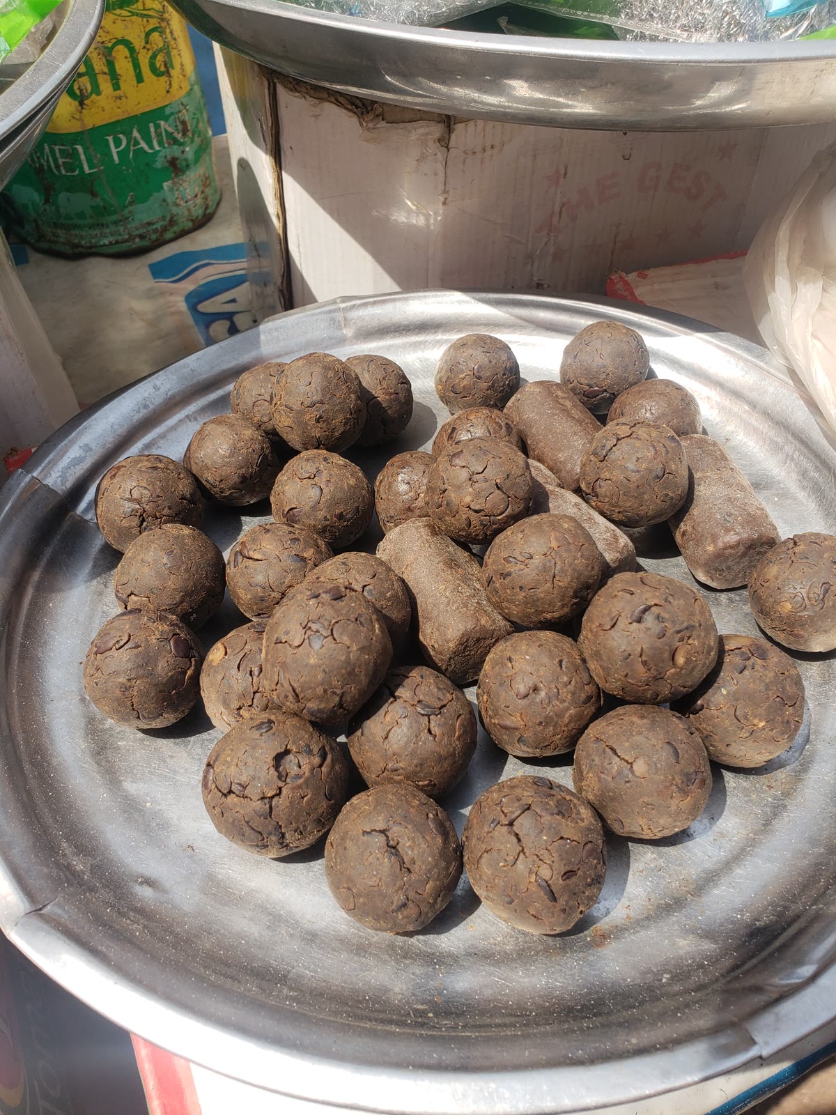 Dark brown balls of fermented dawadawa arranged on a round metal tray in Ghana.