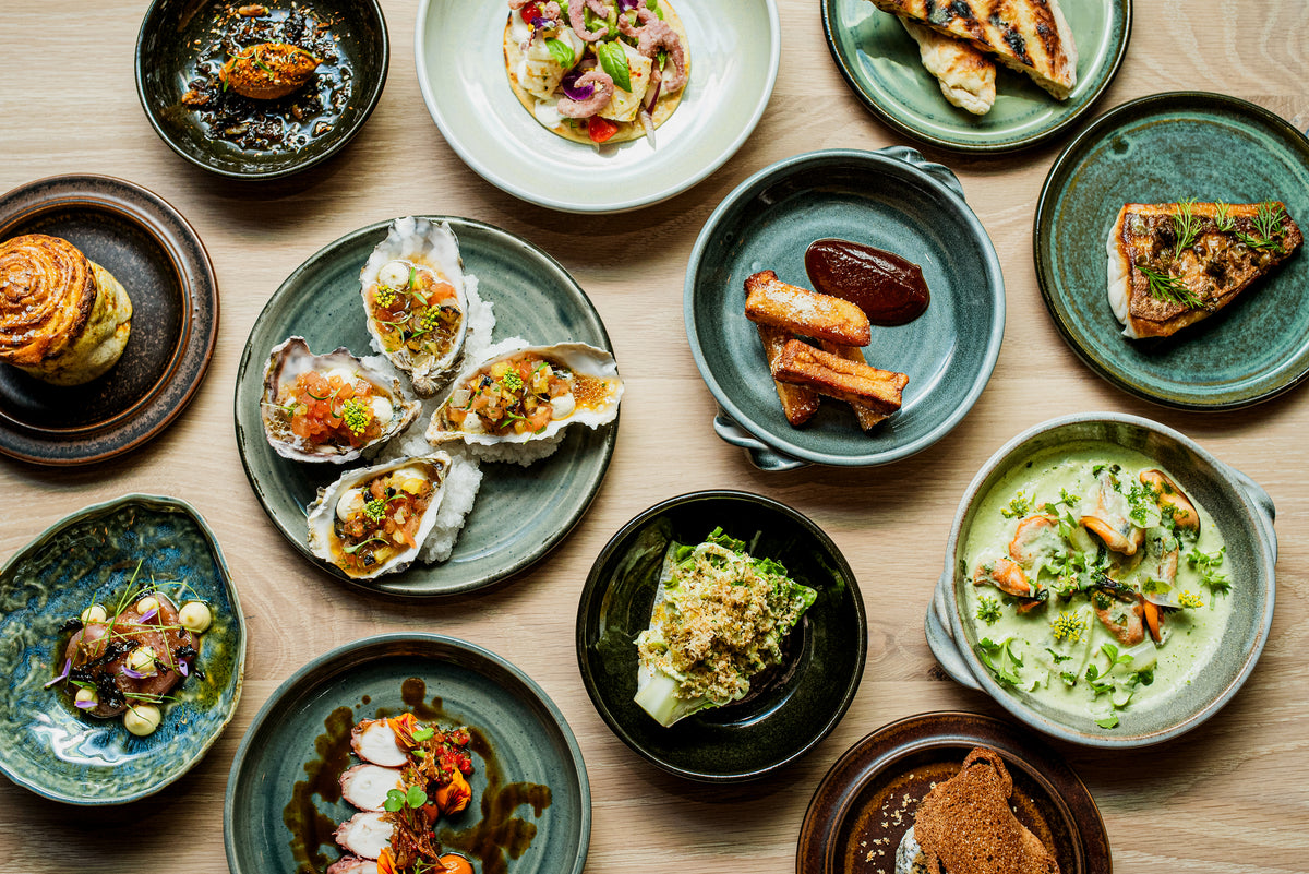 An overhead spread of oysters, grilled fish, shellfish, bread, and vegetable dishes on ceramic plates at Galjoen in Cape Town.