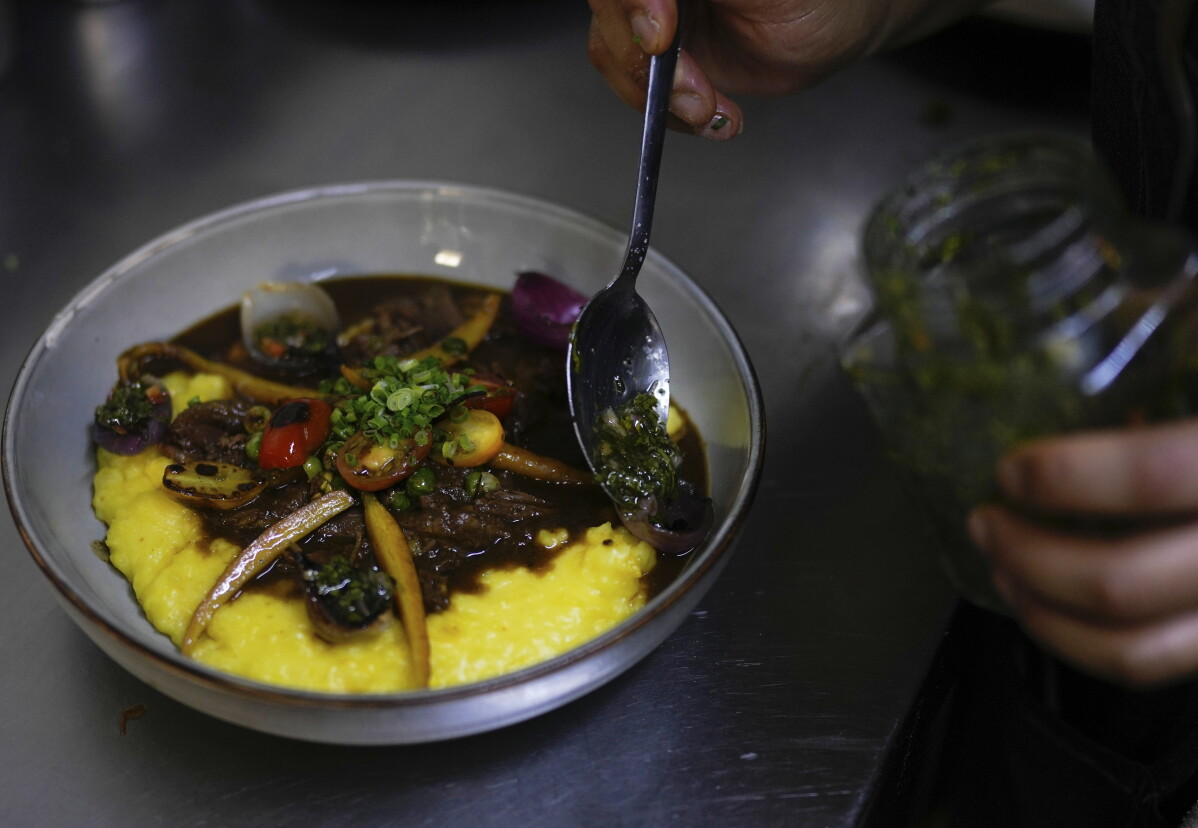 Chef Carolina Chuquimia spoons green herb sauce over beef steak, vegetables and yellow yuca at La Rufina in La Paz.