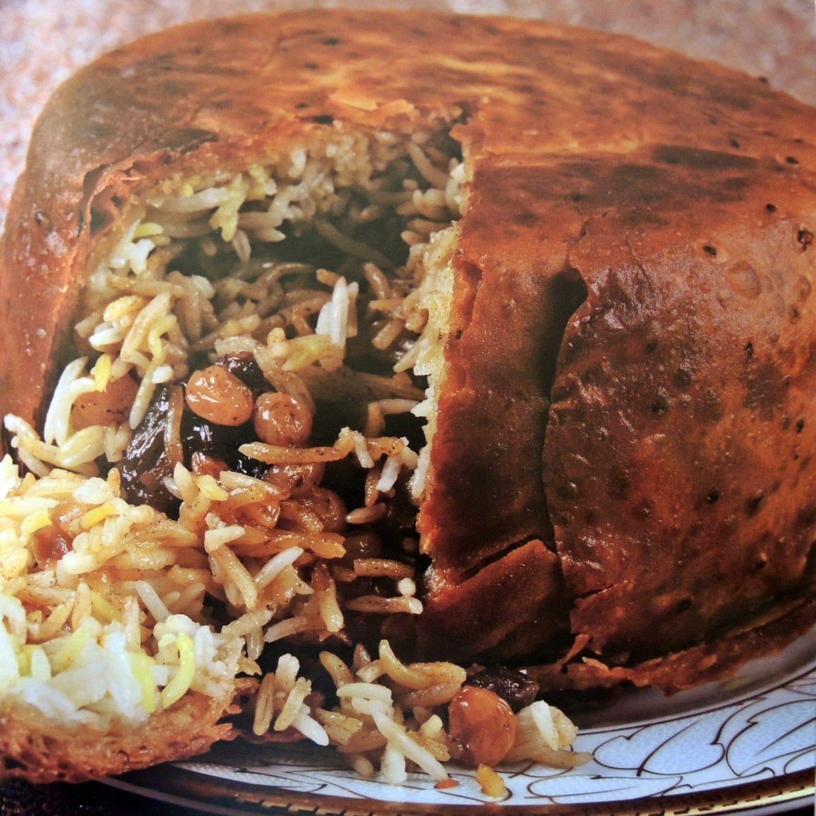 切开一道缺口的圆形 shah plov，深褐面包外壳包裹着长粒米、肉和果干。