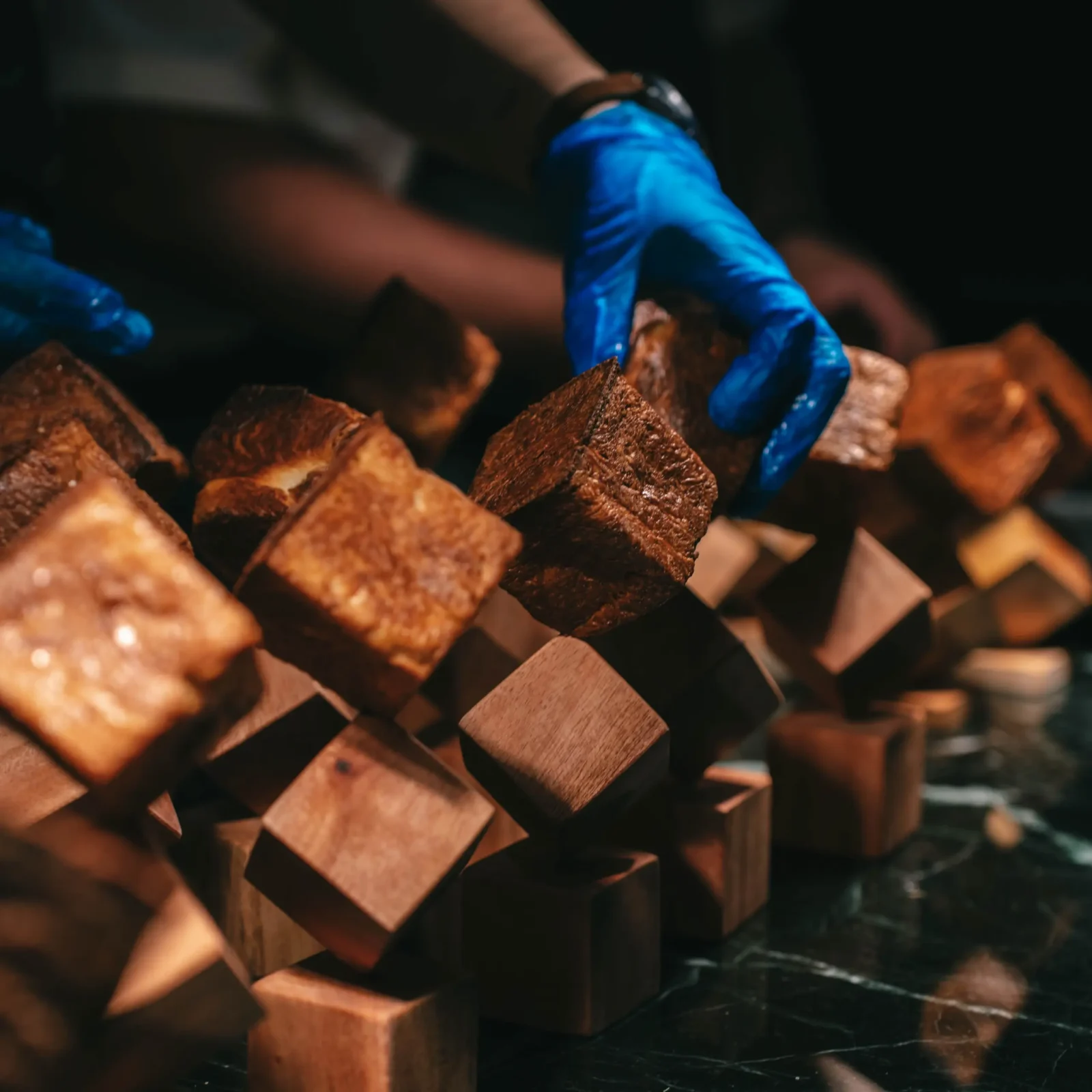 Blue-gloved kitchen hands arrange Tadhana's browned laminated tinigib cornbread on geometric wooden stands.