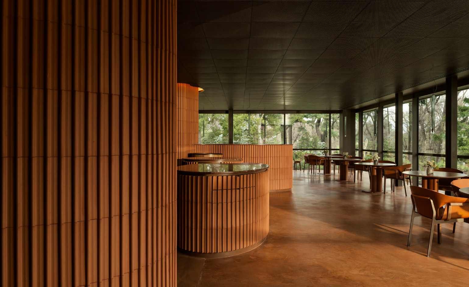 Yiaga's terracotta-lined dining room, with curved ochre walls, timber tables, and windows opening onto Fitzroy Gardens.