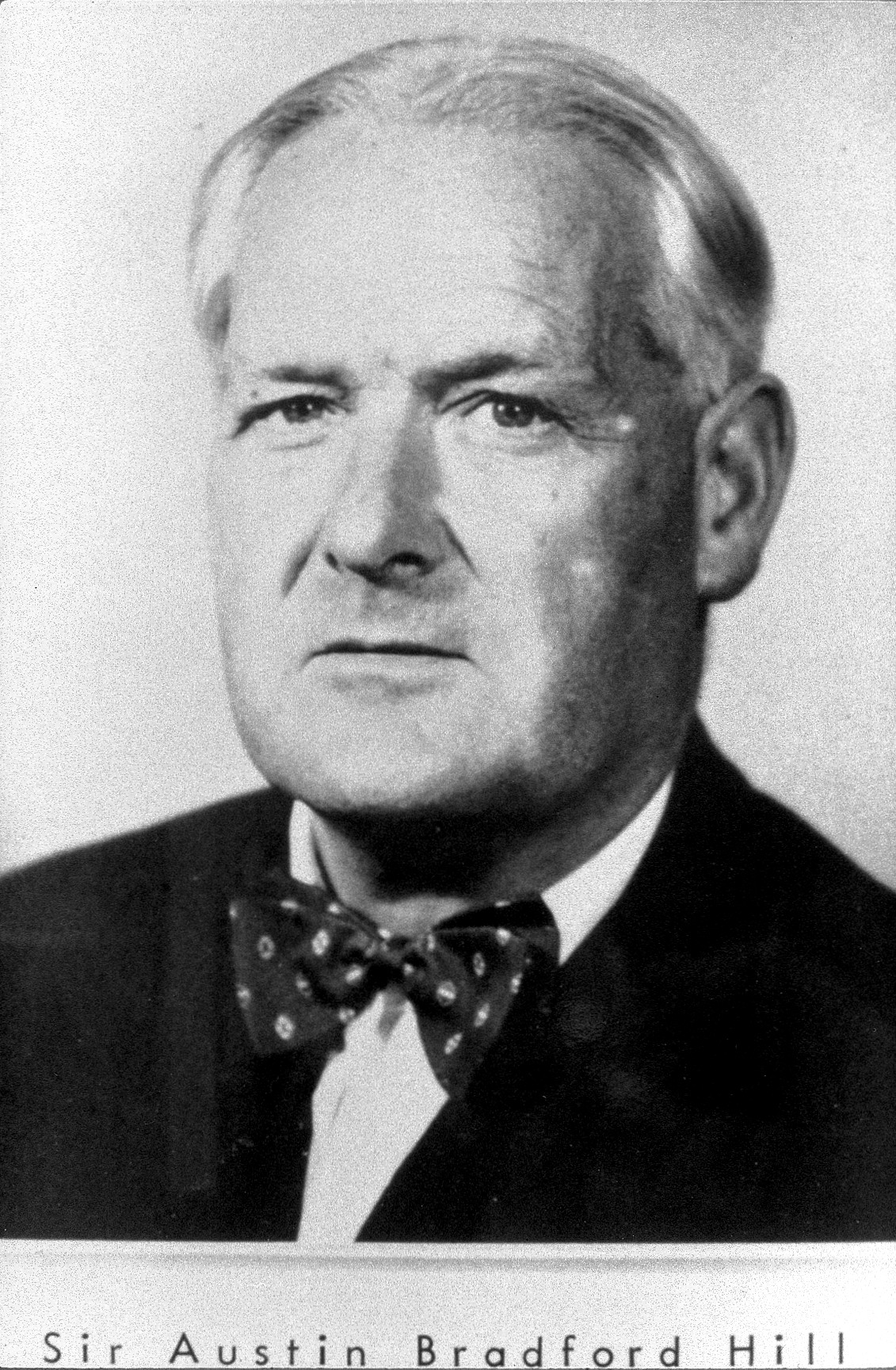 Black-and-white archival portrait of medical statistician Austin Bradford Hill in a dark suit and patterned bow tie.