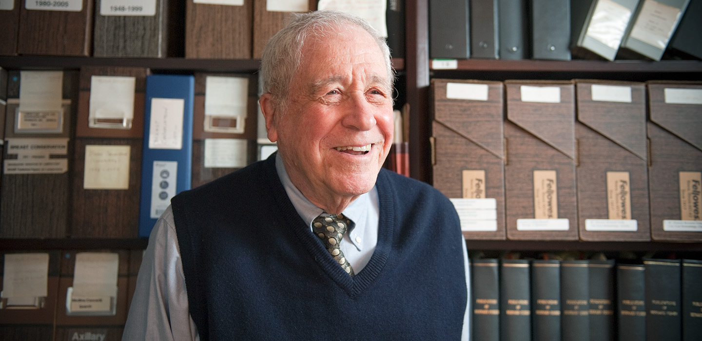Bernard Fisher smiles in his University of Pittsburgh office in front of shelves filled with labeled research files.