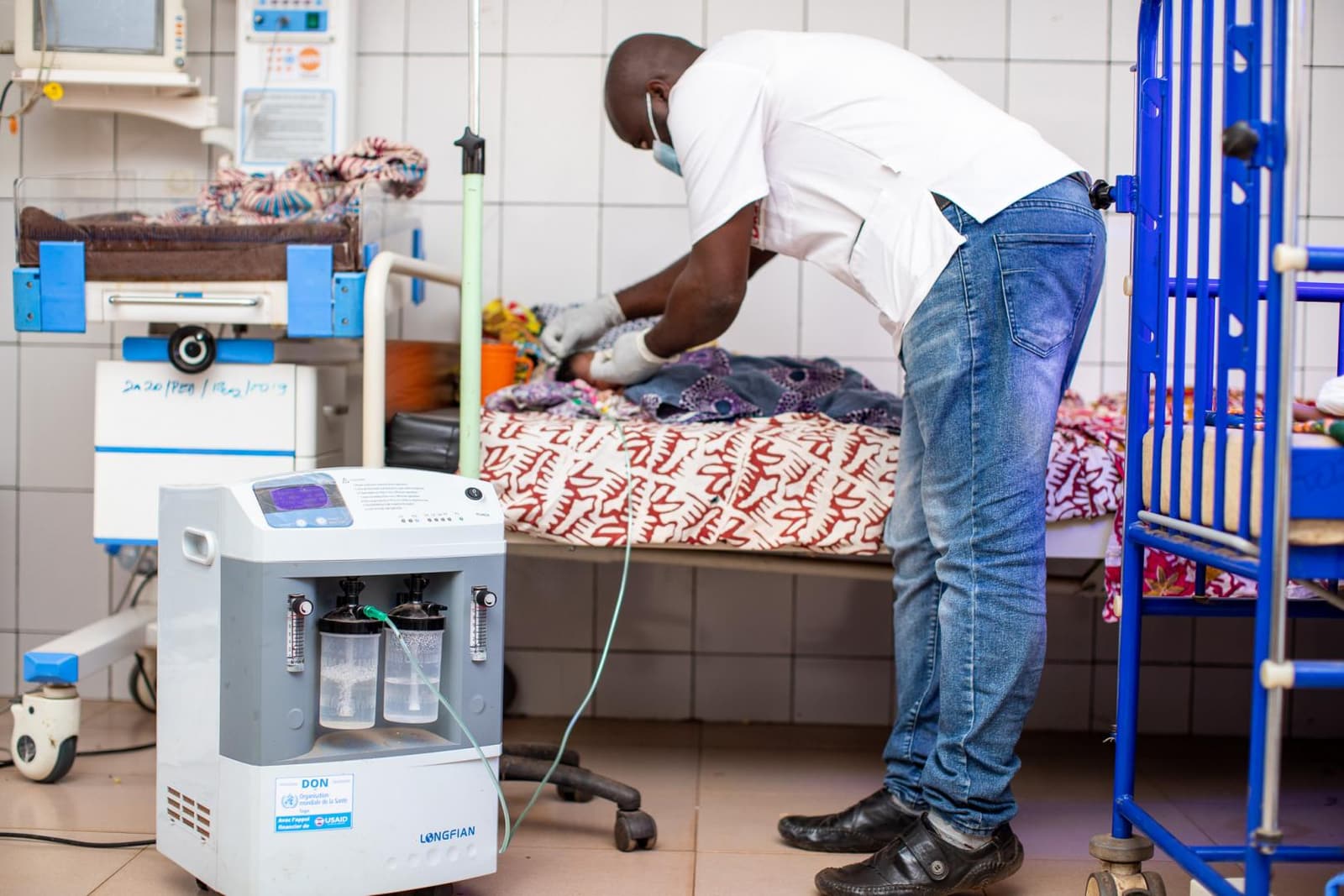 A health worker adjusts oxygen tubing for an infant at Tsévié Regional Hospital in Togo, with a bedside oxygen concentrator in the foreground.