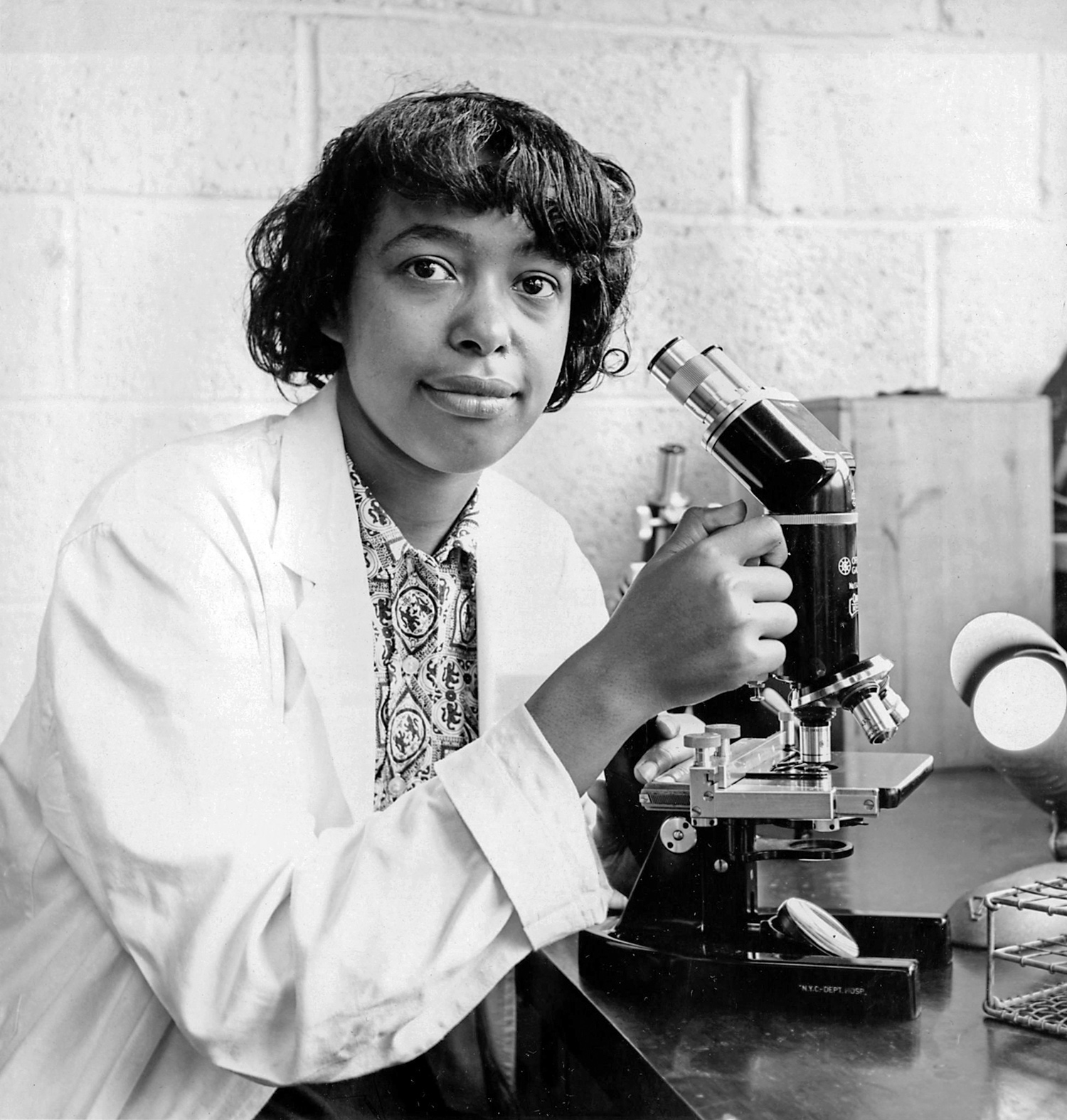 Sixteen-year-old Patricia Bath looks toward the camera while adjusting a microscope during a 1959 summer research program.