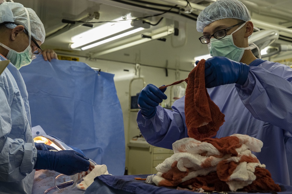 An operating-room specialist holds up a blood-stained Ray-Tec sponge while counting a pile of surgical sponges during a simulated operation.