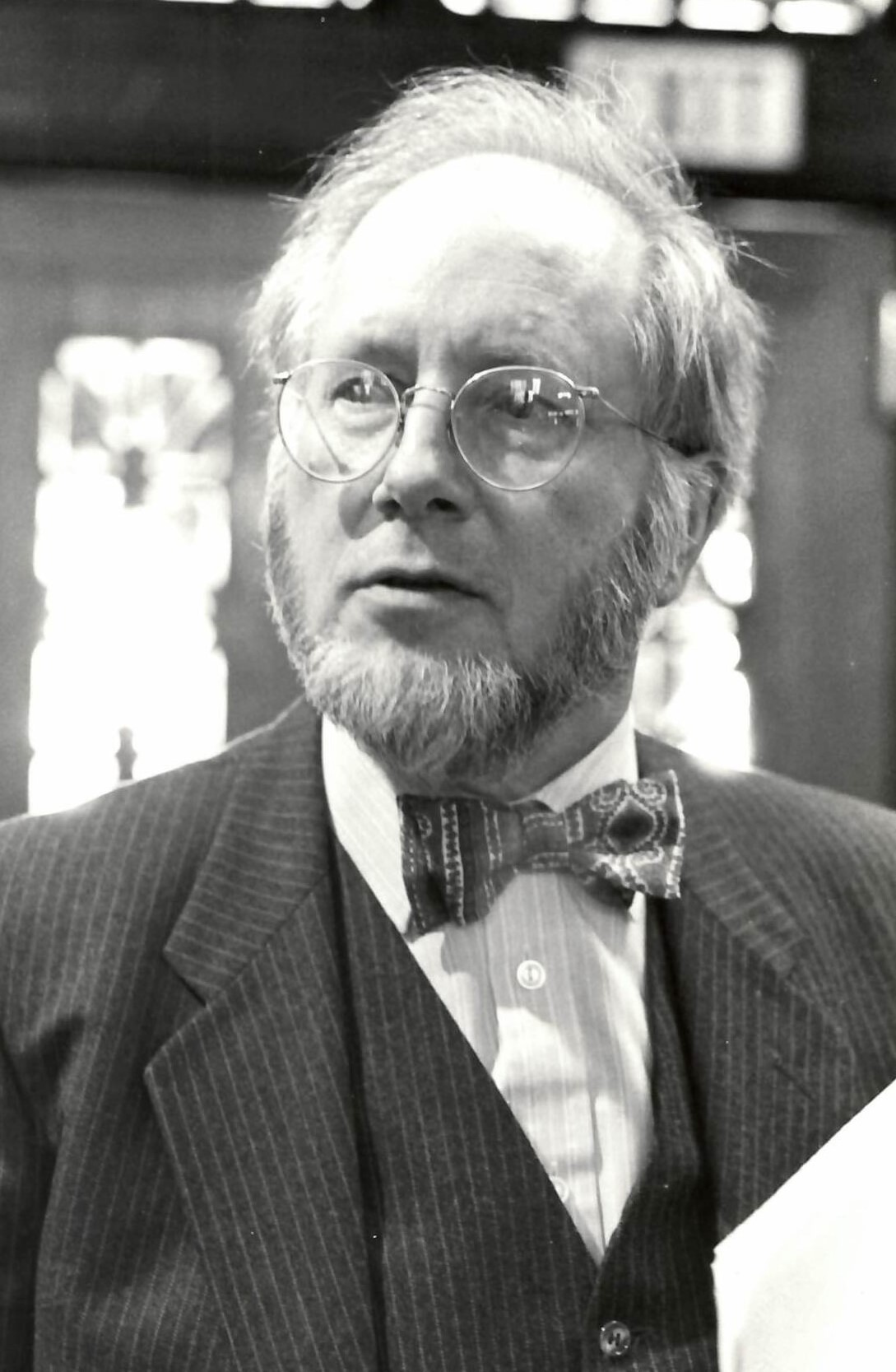 Black-and-white archival portrait of physician and epidemiologist Julian Tudor Hart wearing round glasses and a patterned bow tie.