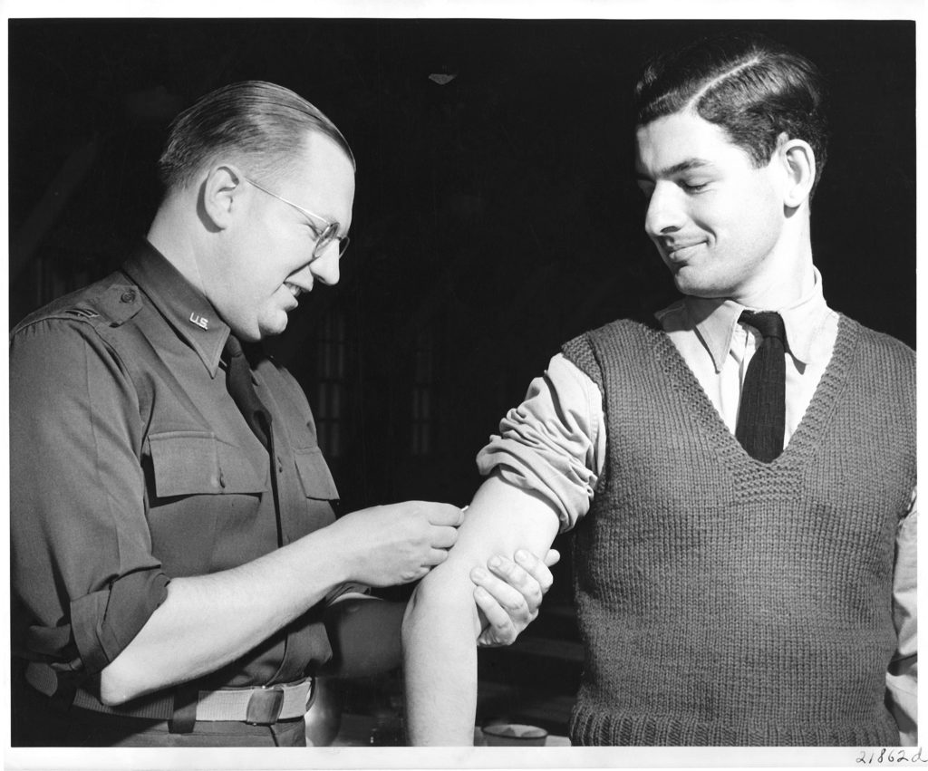 A uniformed U.S. Army medical officer injects yellow fever vaccine into a soldier's exposed upper arm in 1942.