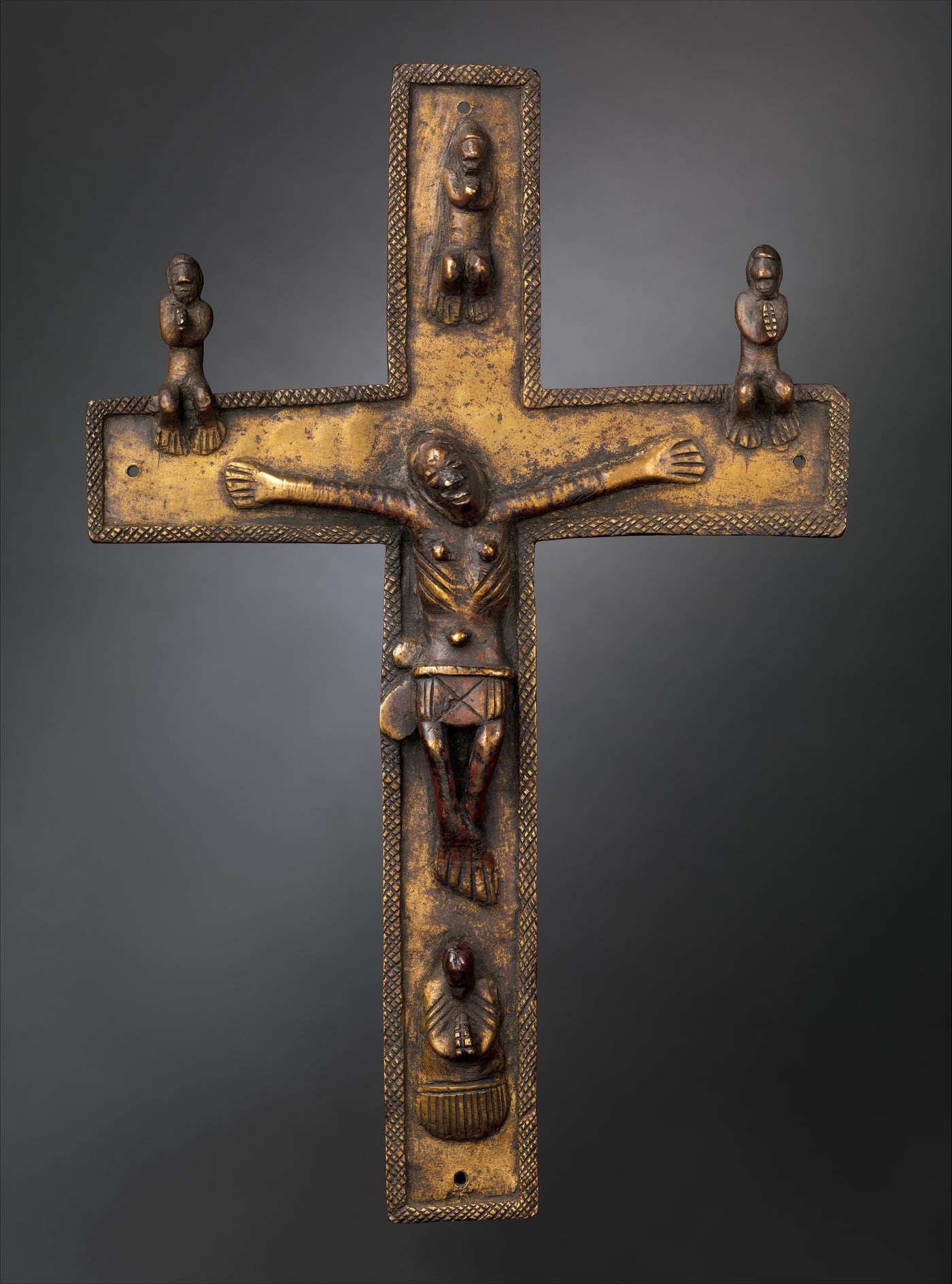 Studio photograph of a worn brass Kongo crucifix with an African Christ figure and four smaller praying figures cast onto the cross.