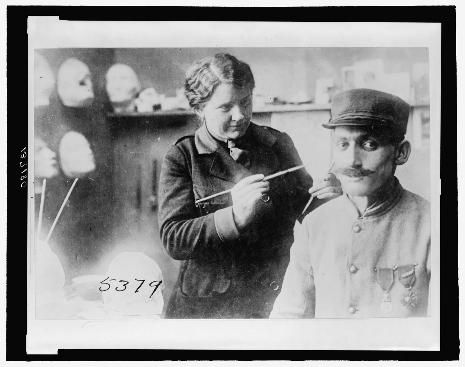 Anna Coleman Ladd uses a brush to paint a facial mask worn by a seated French soldier in her Paris studio in July 1918.