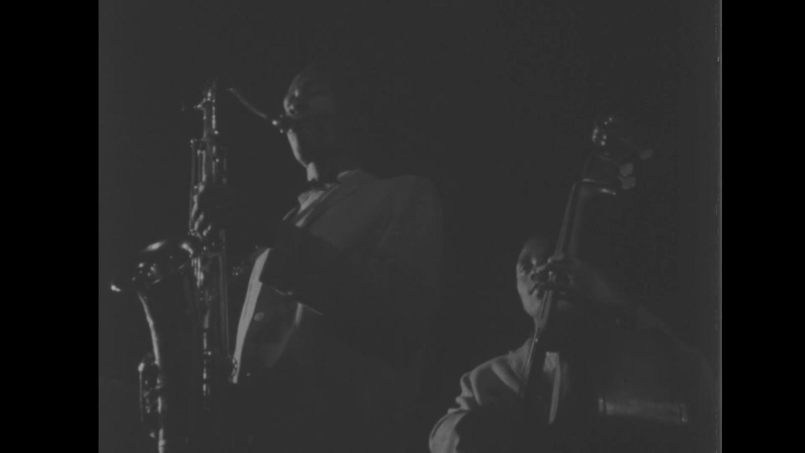 Black-and-white archival film frame showing a saxophonist and double bassist from Sun Ra's Arkestra performing in Chicago.