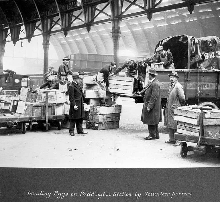 Black-and-white archival photograph of volunteer porters loading wooden crates of eggs onto carts and a truck at Paddington Station during the 1926 General Strike.