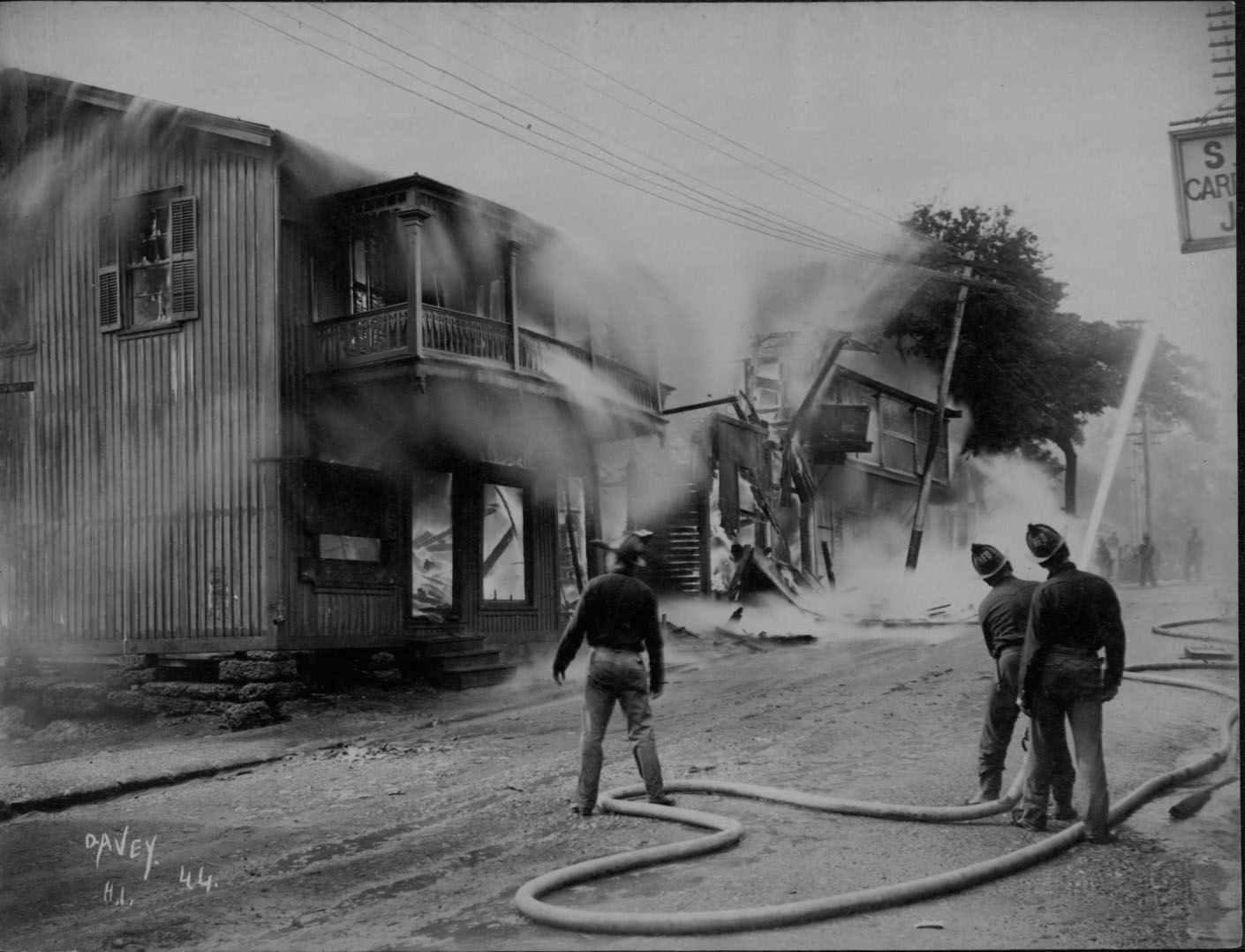 Firefighters direct hoses toward smoke-filled wooden buildings during Honolulu's 1900 Chinatown fire.