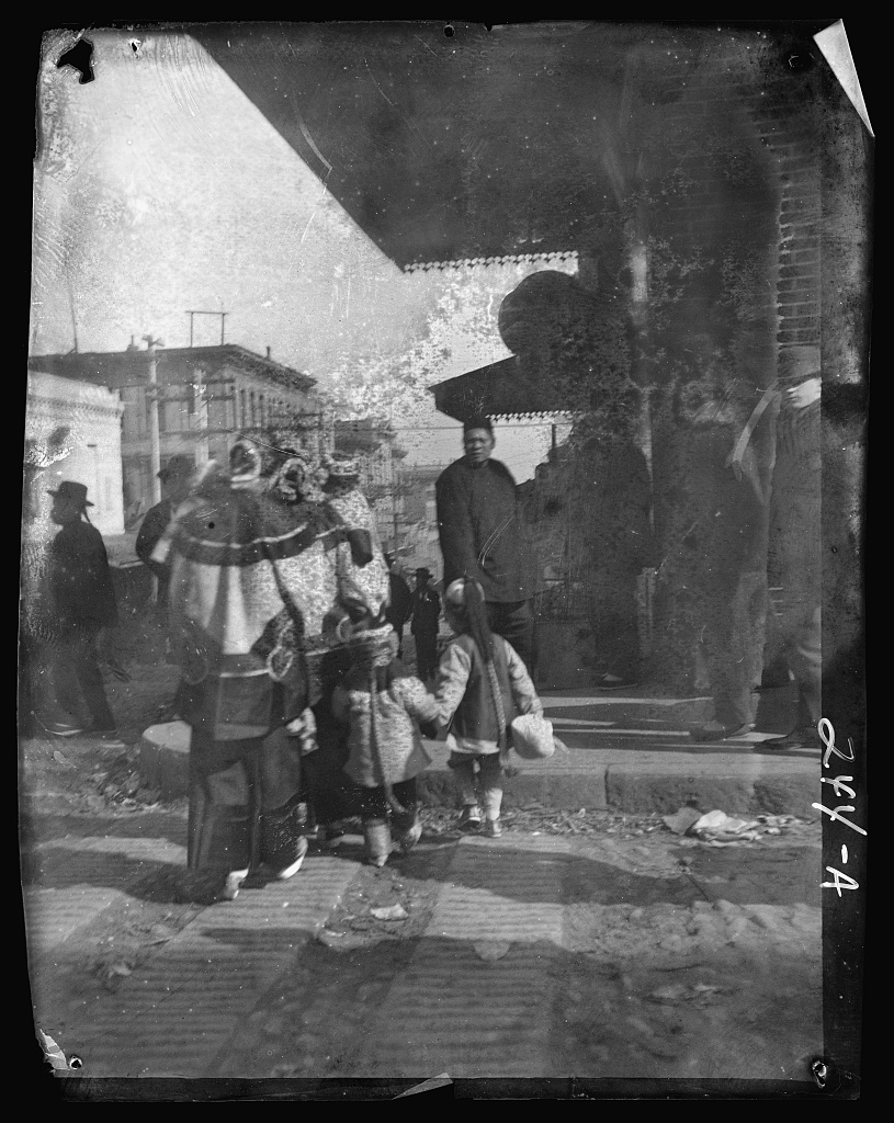 Damaged black-and-white negative photograph of women and children crossing a street in San Francisco's Chinatown around the turn of the twentieth century.